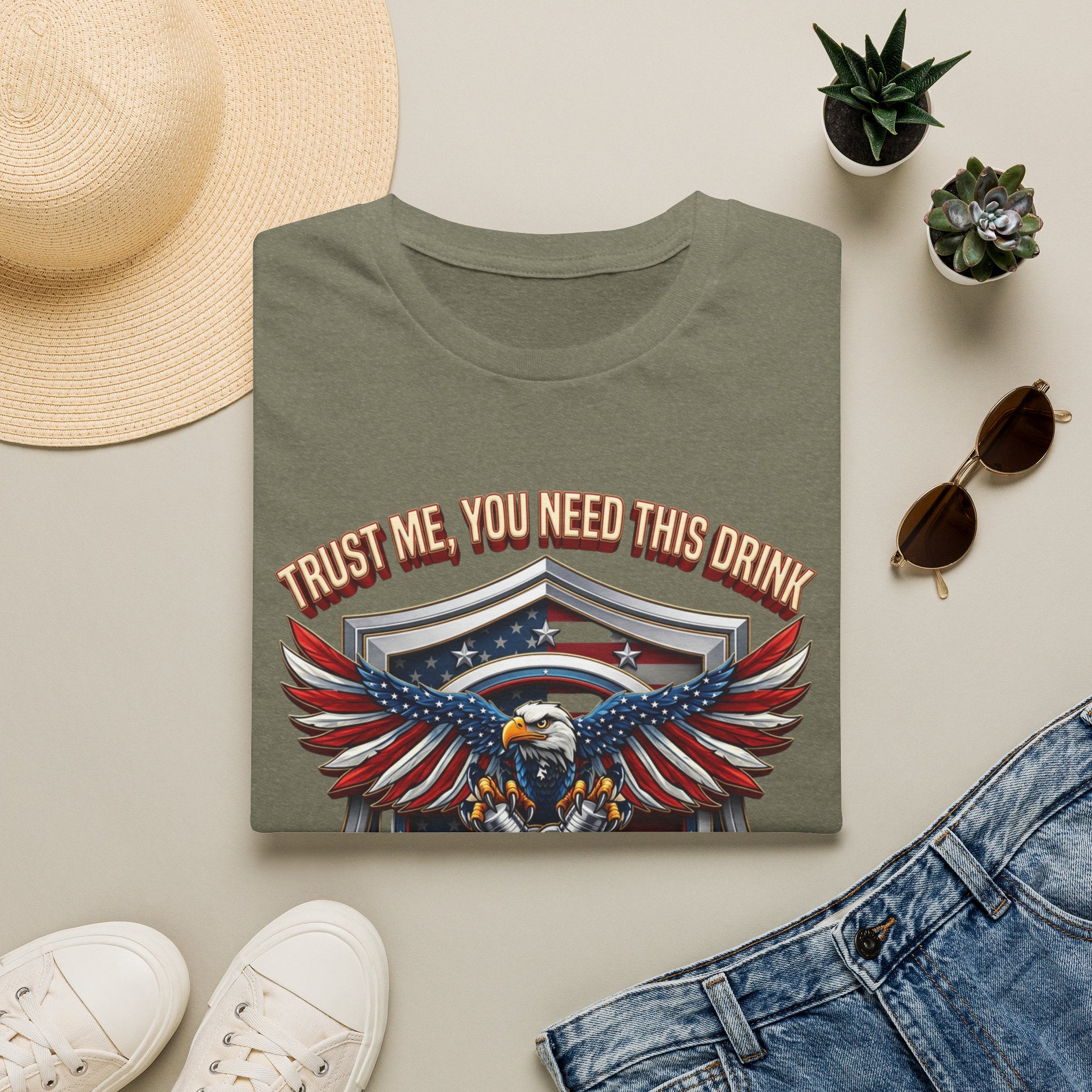 Bartender Eagle Trust Me You Need This Drink print on a Heather Military Green t-shirt, folded beside a straw hat and jeans