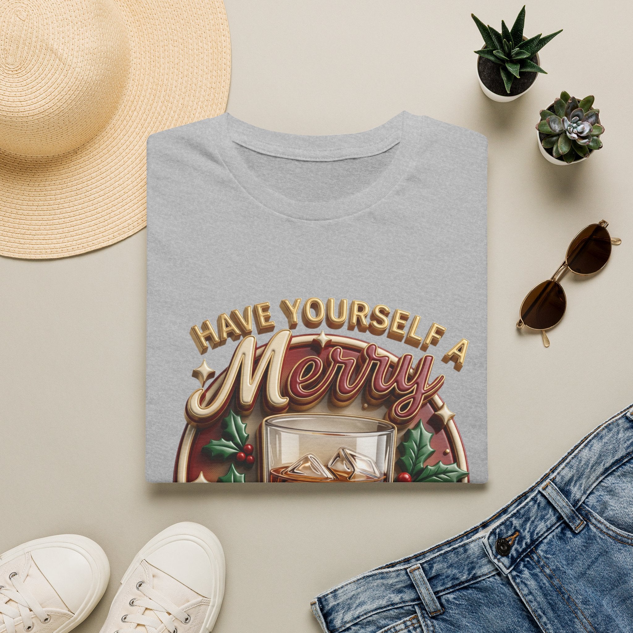 Have Yourself a Merry Little Cocktail print on a Sport Grey t-shirt, folded beside a straw hat and jeans