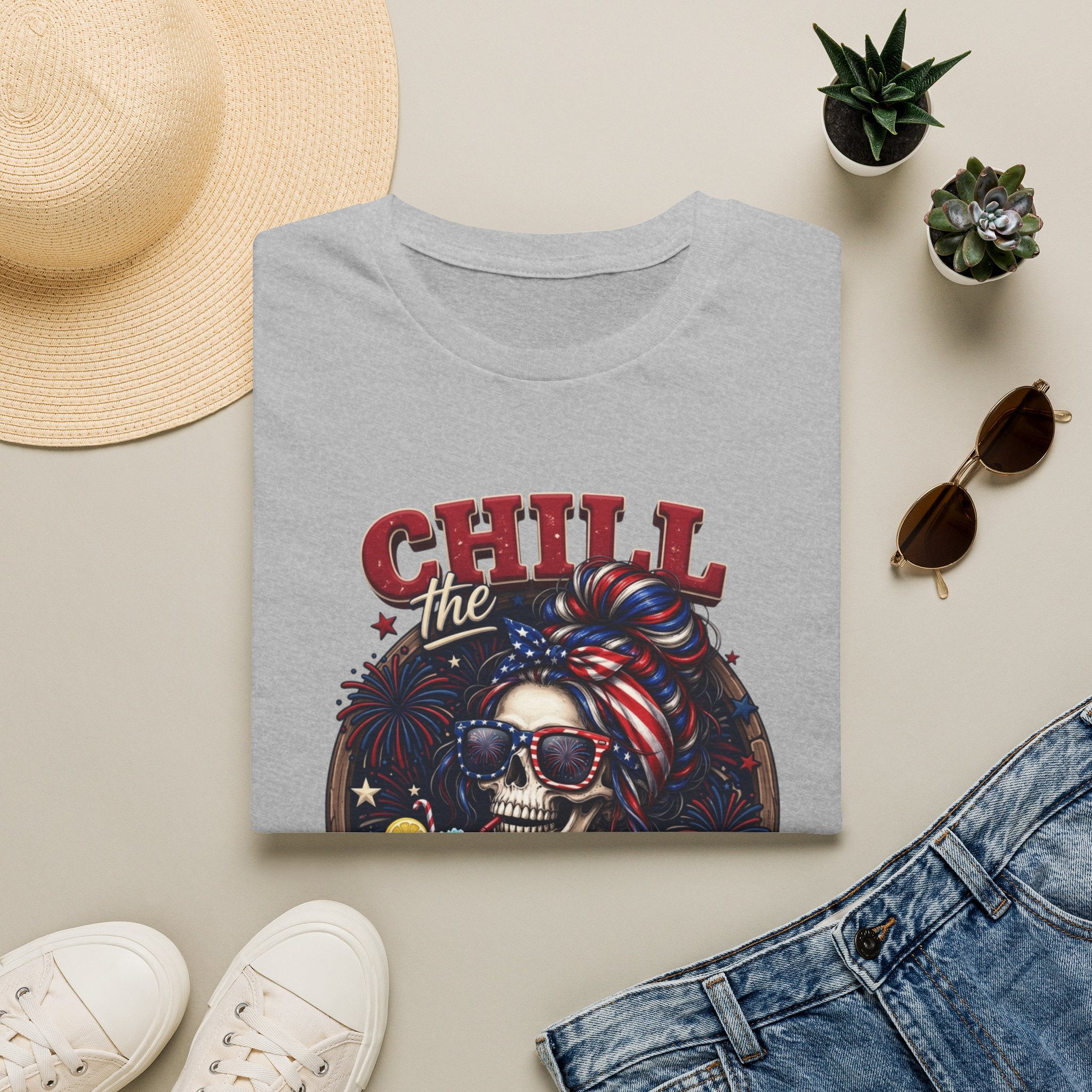 Chill the Fourth Out Patriotic Skeleton 4th of July print on a Sport Grey t-shirt, folded beside a straw hat and jeans