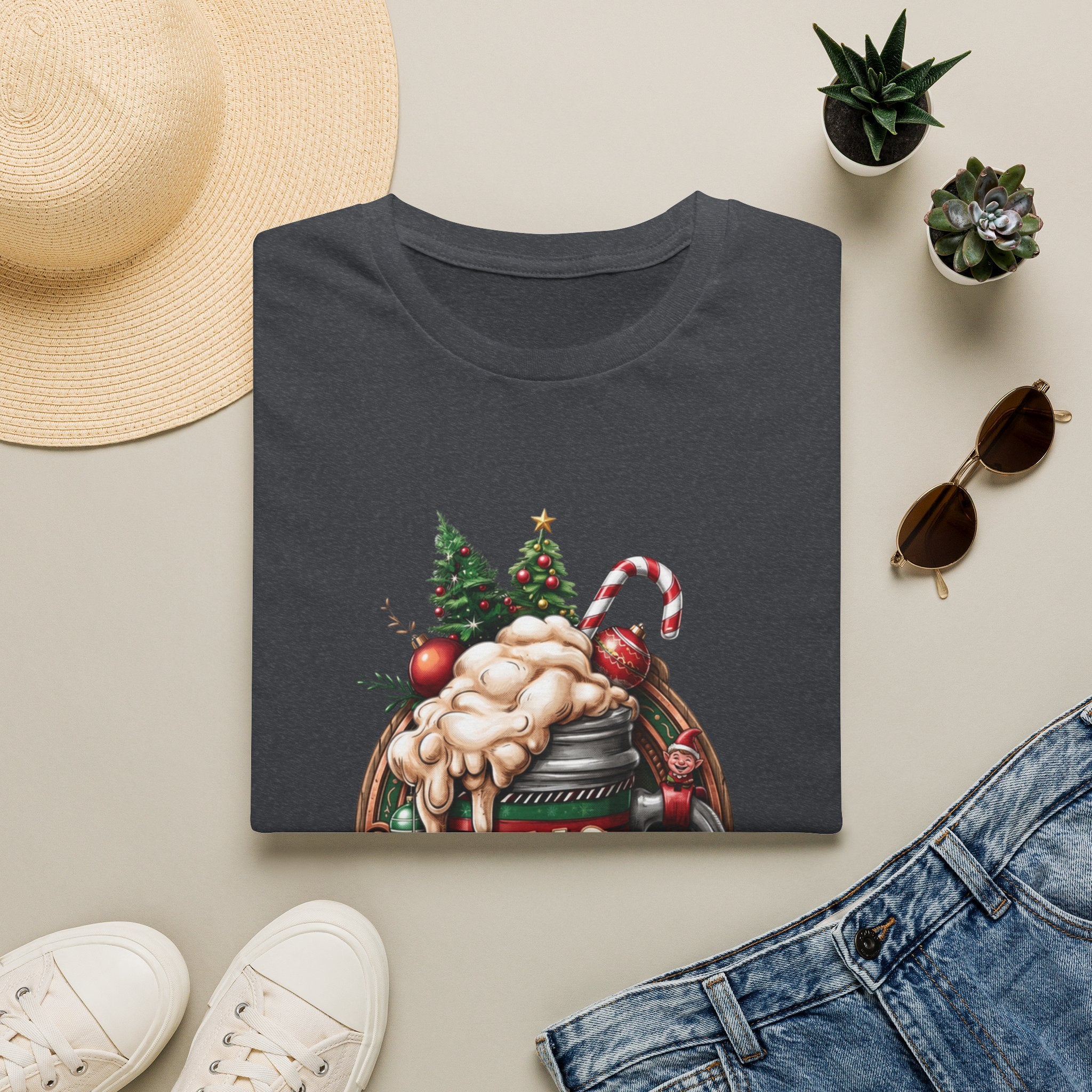 XMAS Beer Pour Me a Very Merry Christmas print on a Dark Heather Grey t-shirt, folded beside a straw hat and jeans
