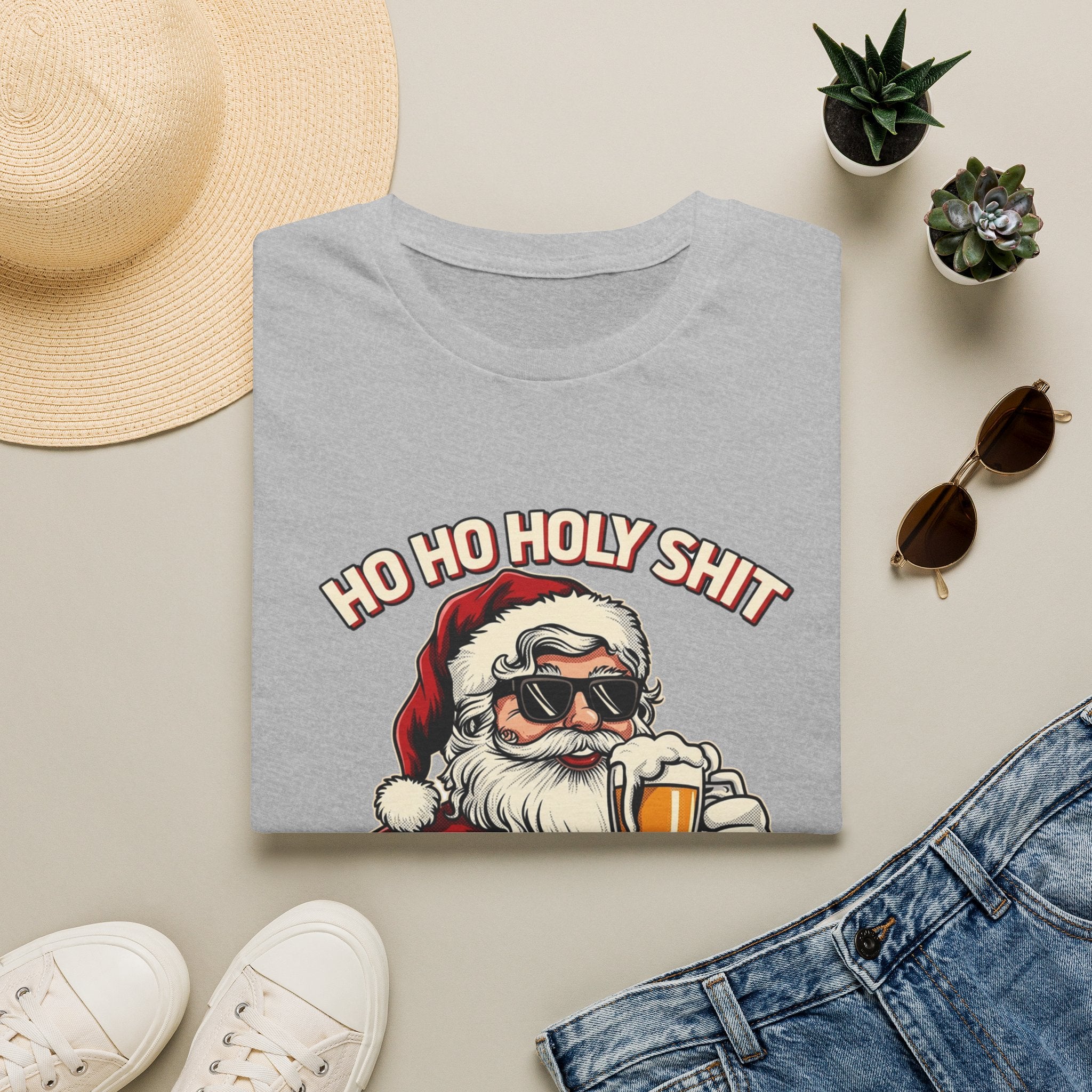 Ho Ho Holy Sh*t I Need a Beer print on a Sport Grey t-shirt, folded beside a straw hat and jeans