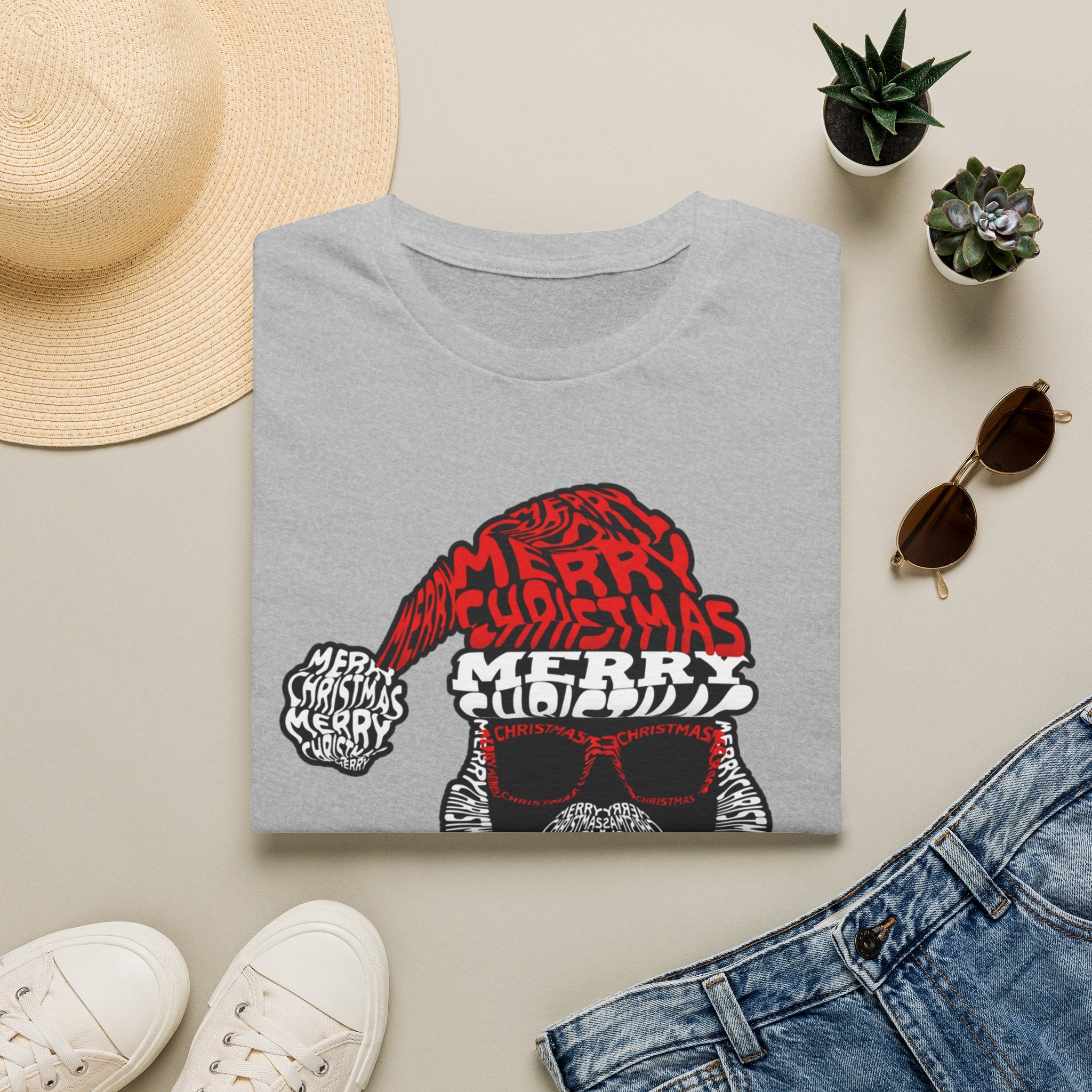 Cool Santa Sunglasses Typography Merry print on a Sport Grey t-shirt, folded beside a straw hat and jeans