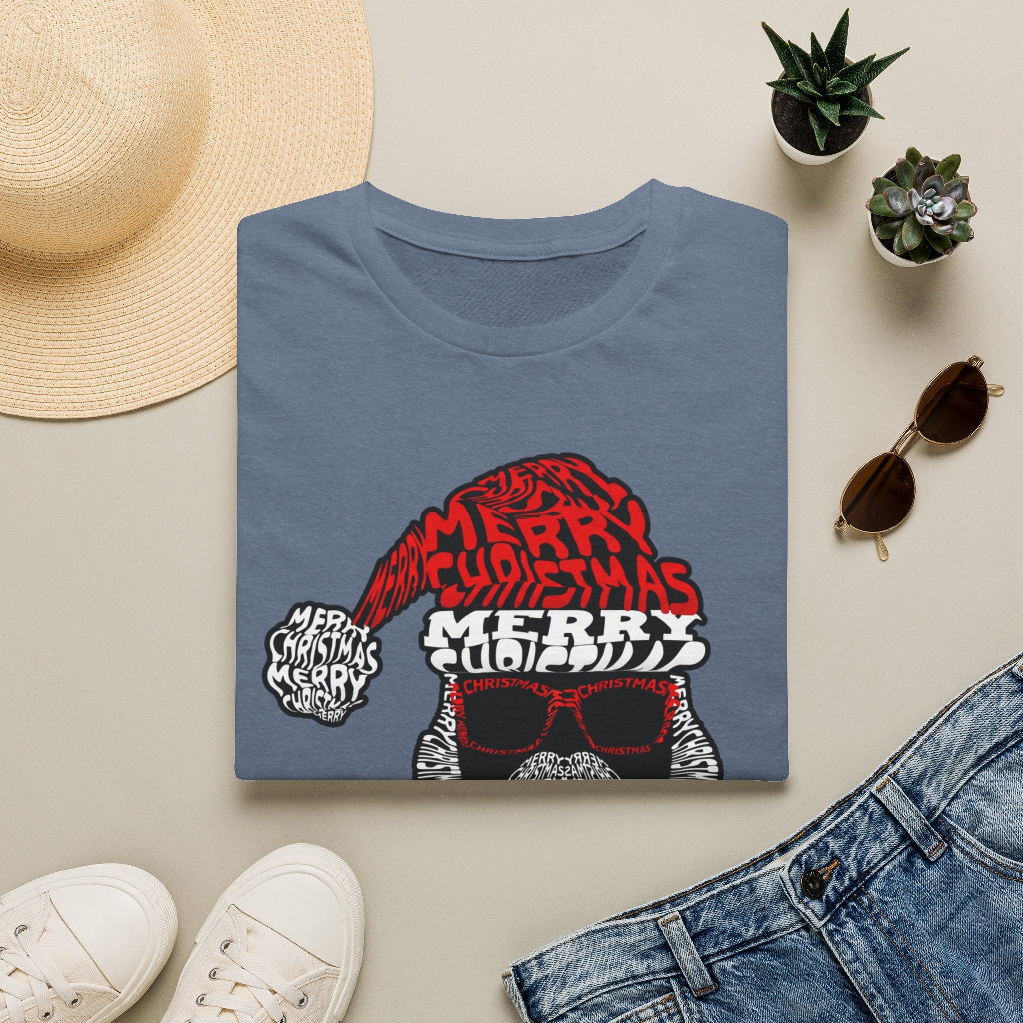 Cool Santa Sunglasses Typography Merry print on a Heather Indigo t-shirt, folded beside a straw hat and jeans