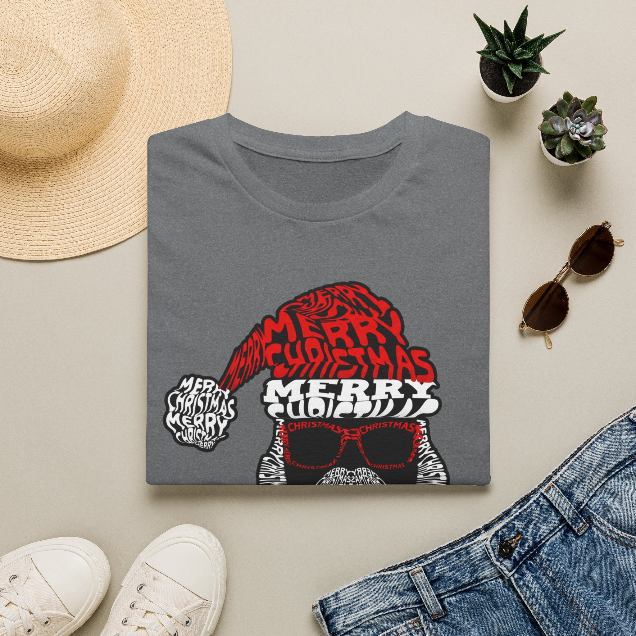 Cool Santa Sunglasses Typography Merry print on a Graphite Heather t-shirt, folded beside a straw hat and jeans