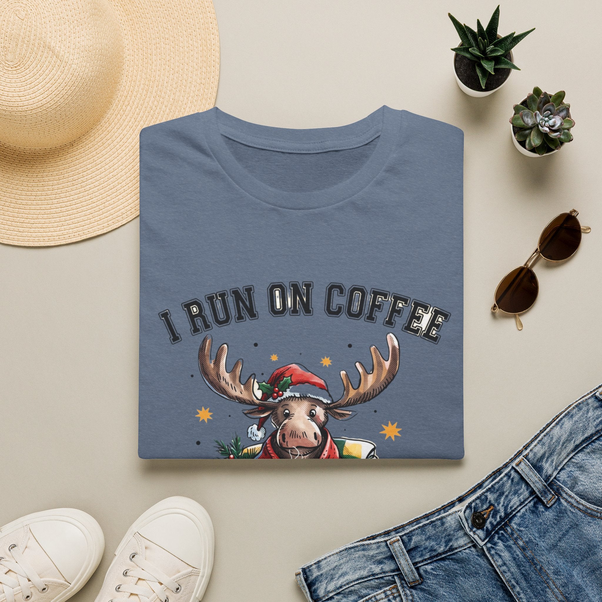 Moose I Run On Coffee and Sleighin' It print on a Heather Indigo t-shirt, folded beside a straw hat and jeans