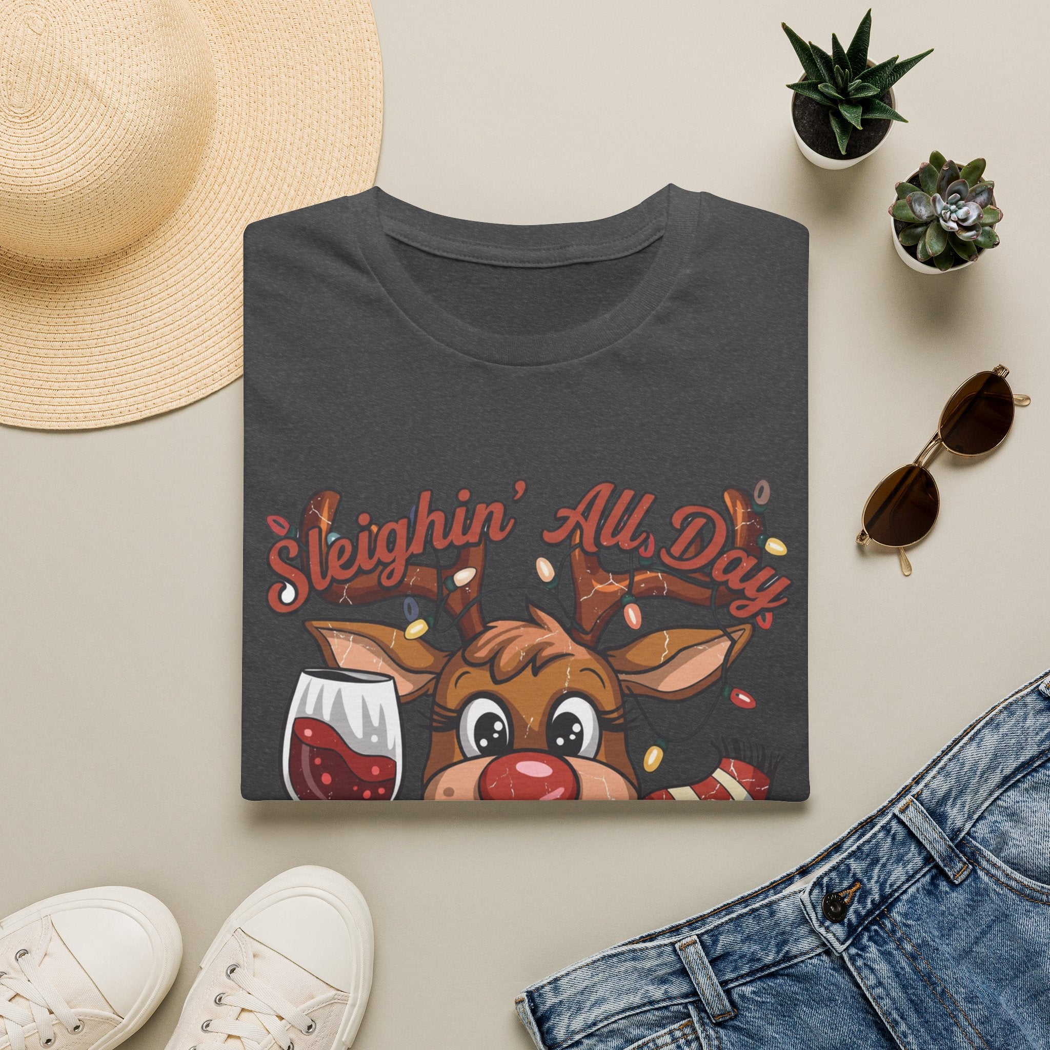 Reindeer Sleighin' All Day Tipsy All Night print on a Dark Heather t-shirt, folded beside a straw hat and jeans