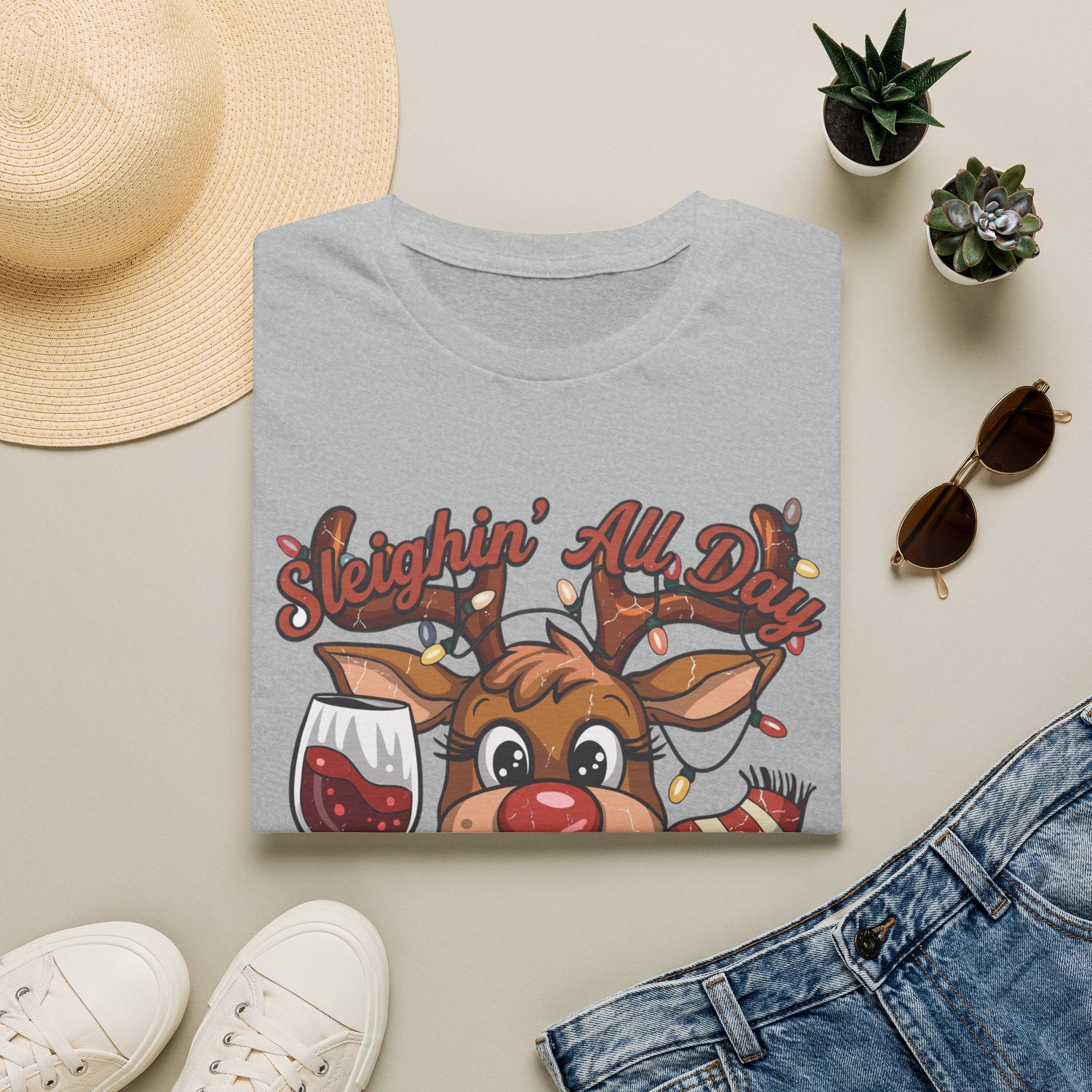 Reindeer Sleighin' All Day Tipsy All Night print on a Sport Grey t-shirt, folded beside a straw hat and jeans