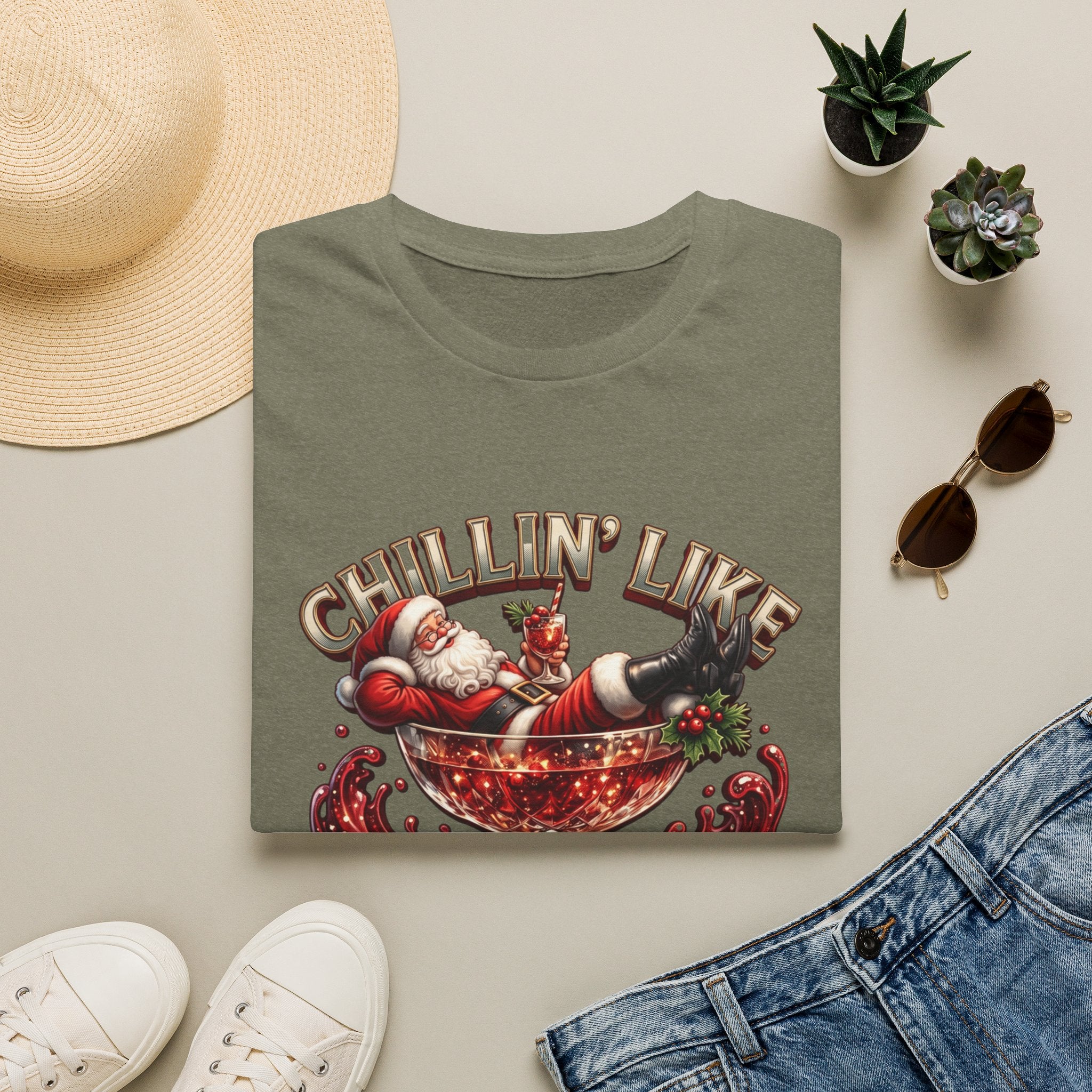 Chillin' Like a Kringle Santa print on a Heather Military Green t-shirt, folded beside a straw hat and jeans