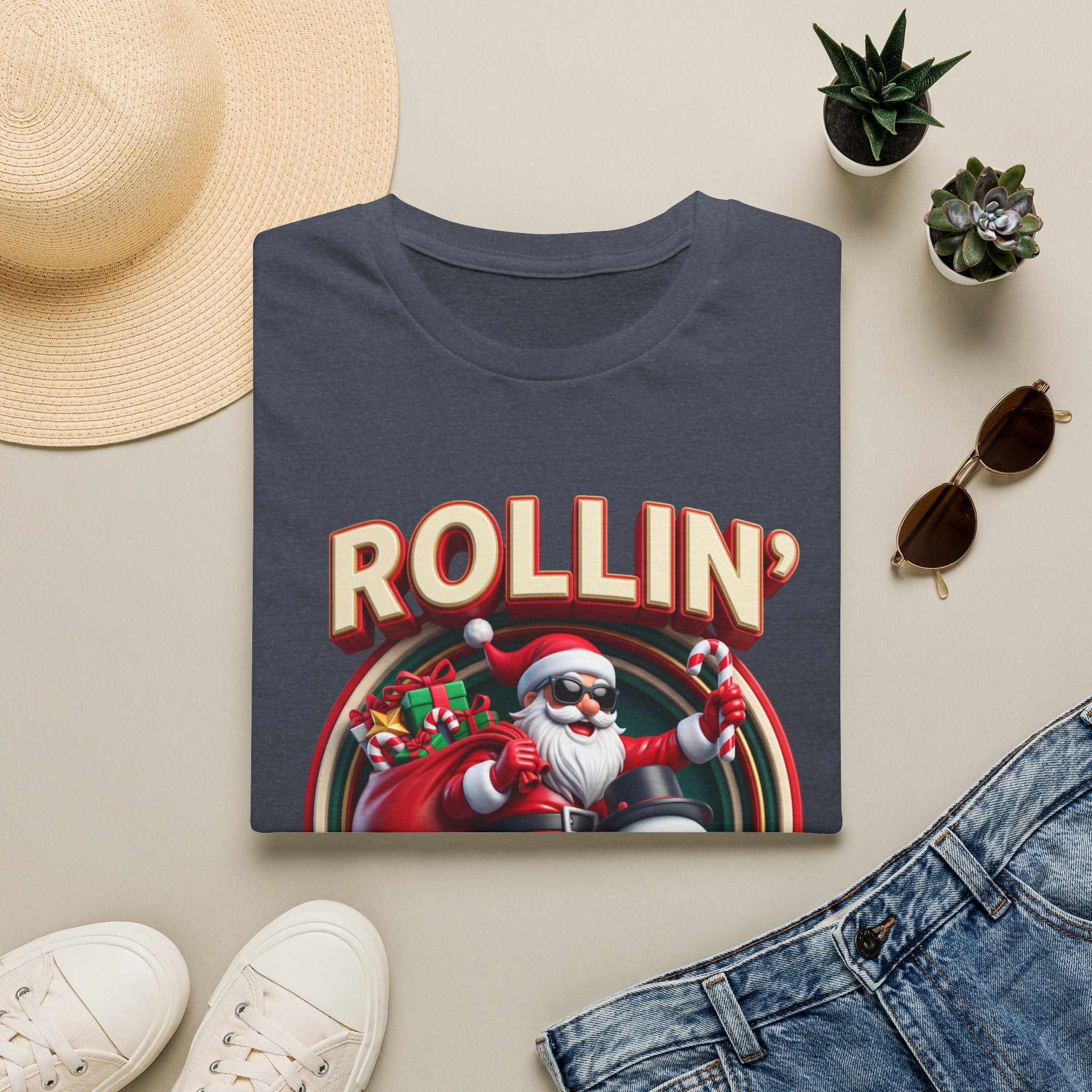 Rollin' with My Snowmies Santa & Snowman print on a Heather Navy t-shirt, folded beside a straw hat and jeans