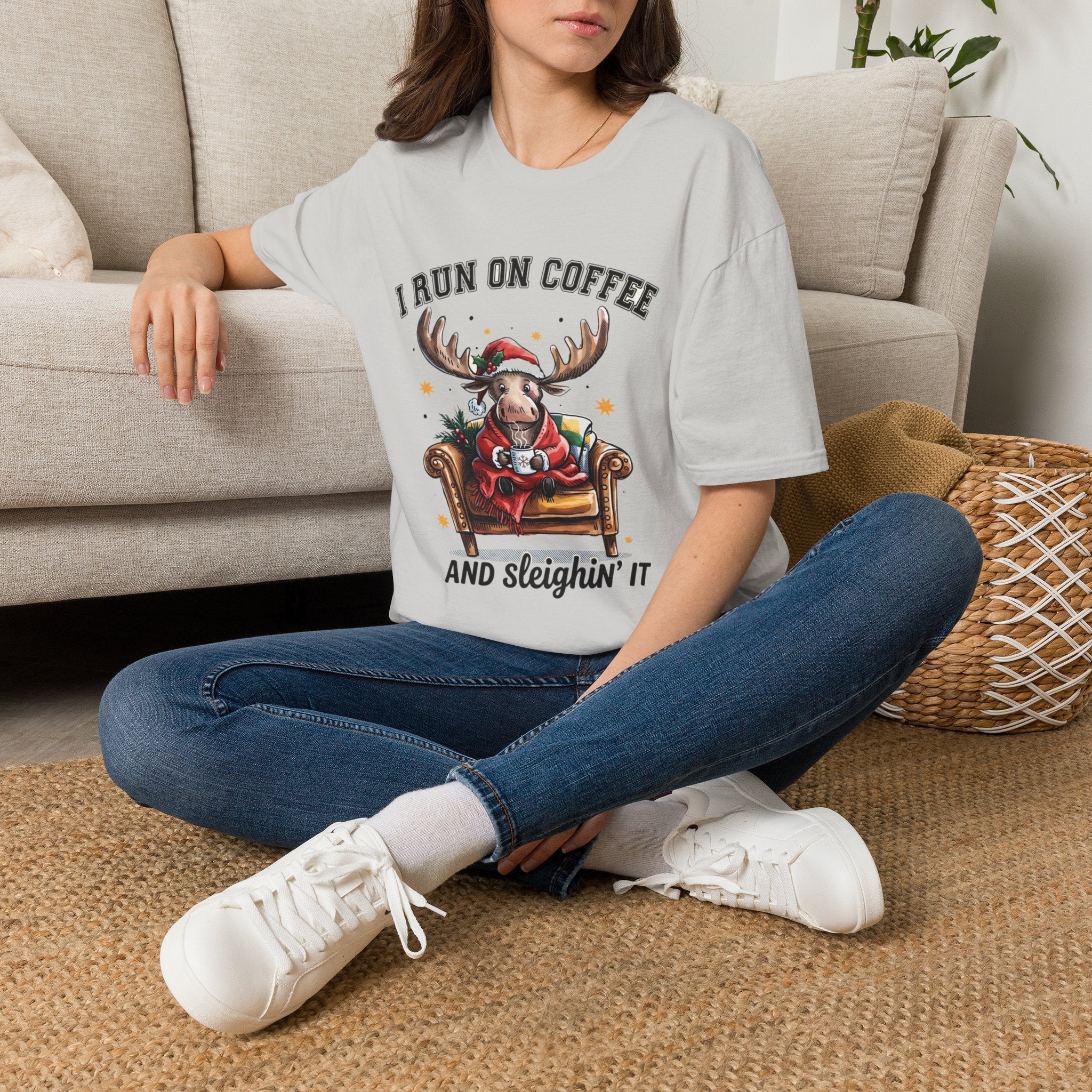 Moose I Run On Coffee and Sleighin' It t-shirt in Ice Grey, worn by a woman seated on a rug