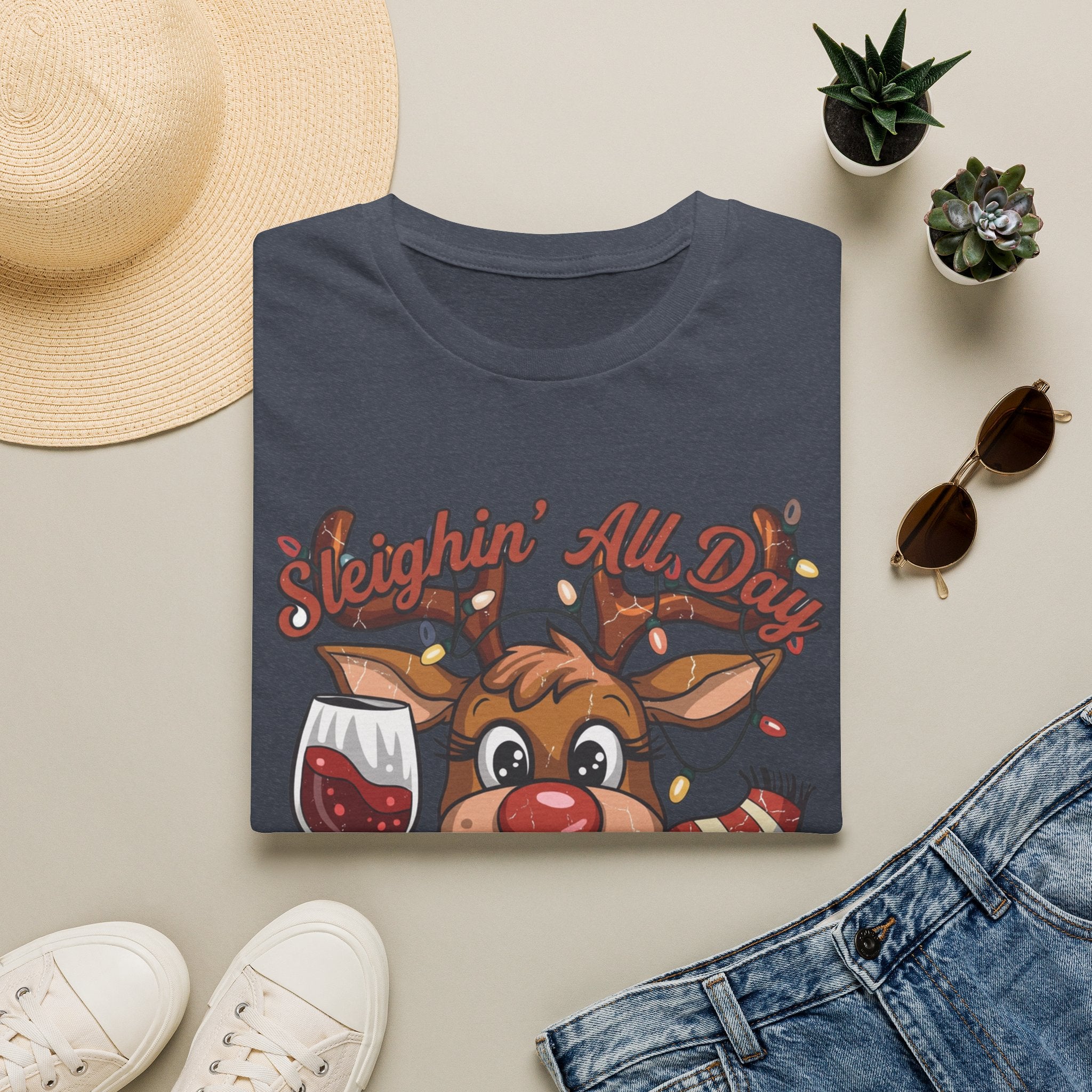 Reindeer Sleighin' All Day Tipsy All Night print on a Heather Navy t-shirt, folded beside a straw hat and jeans
