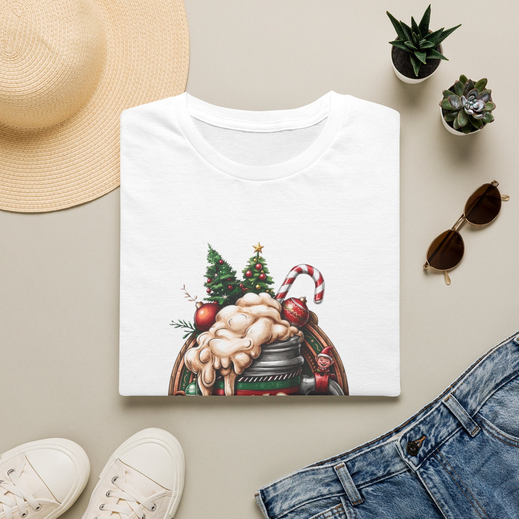 XMAS Beer Pour Me a Very Merry Christmas print on a White t-shirt, folded beside a straw hat and jeans