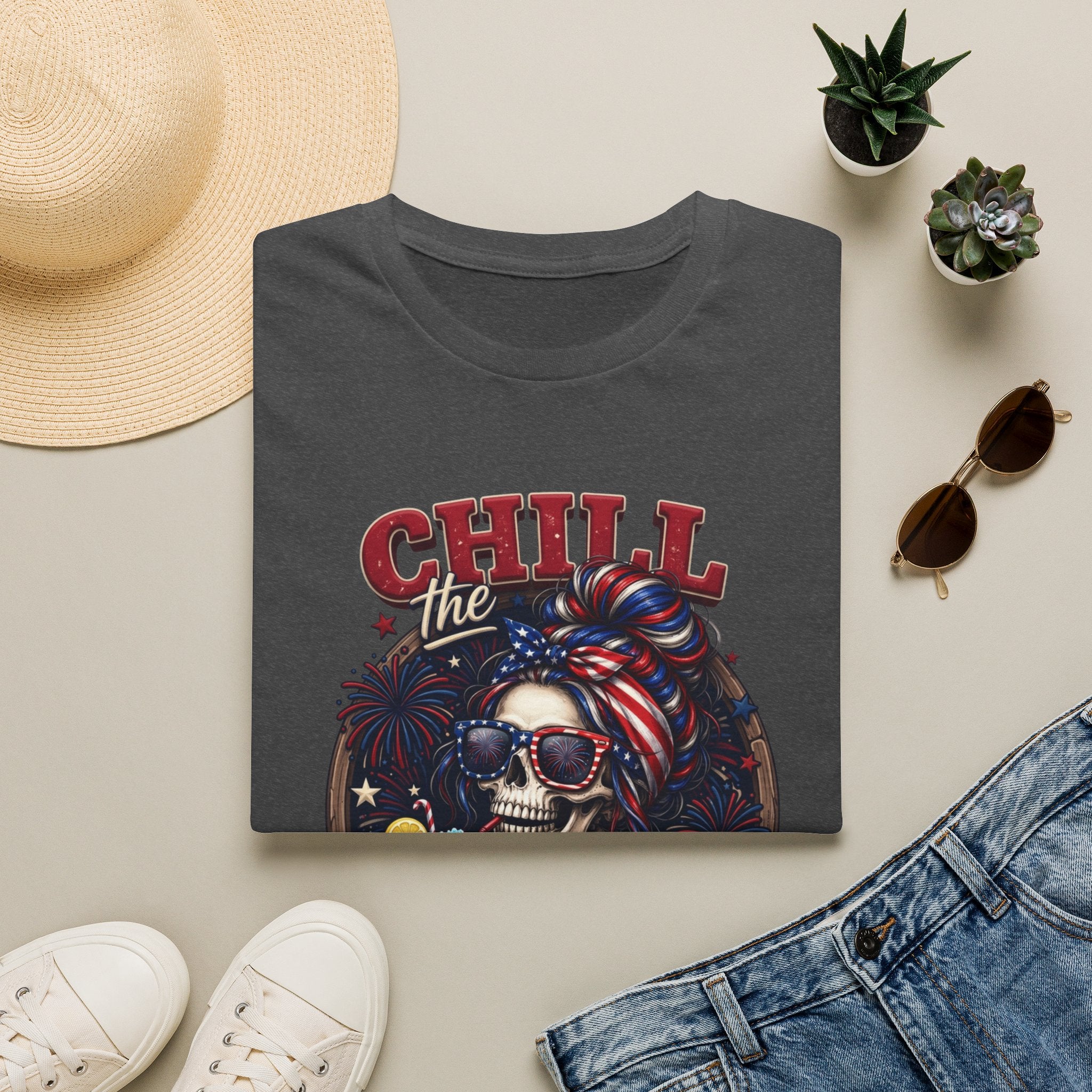 Chill the Fourth Out Patriotic Skeleton 4th of July print on a Dark Heather t-shirt, folded beside a straw hat and jeans