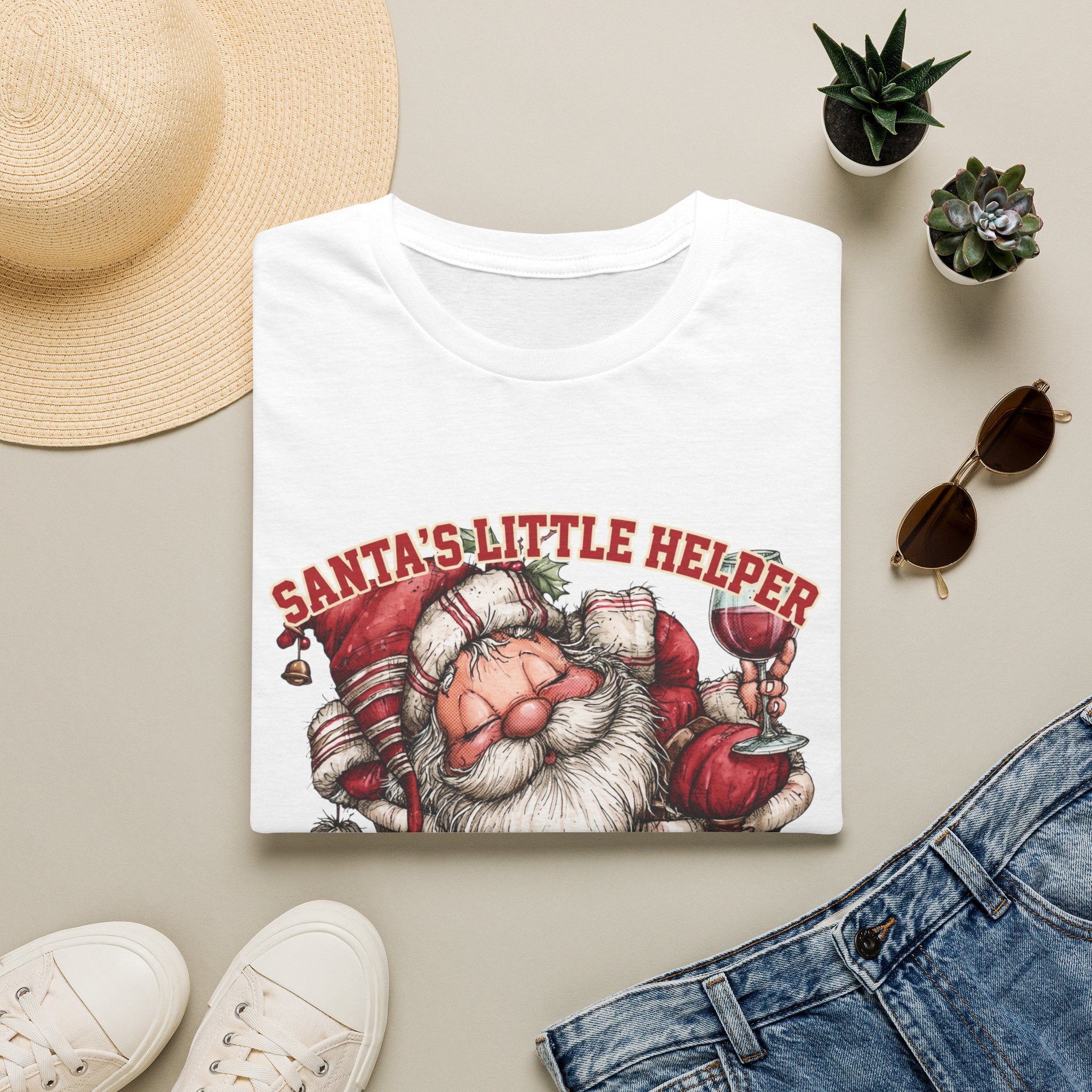 Santa's Little Helper Is Lit Christmas Wine print on a White t-shirt, folded beside a straw hat and jeans