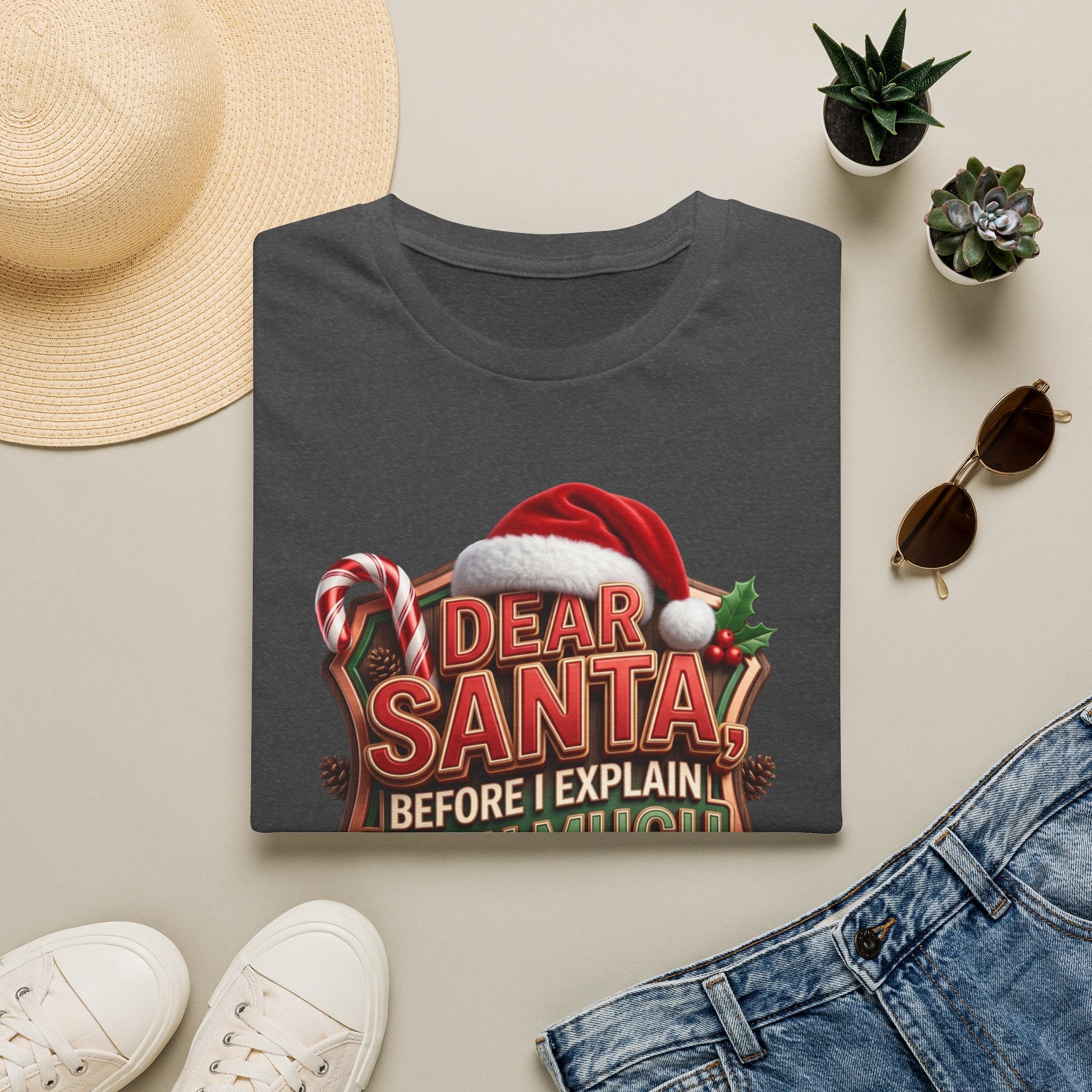 Dear Santa Before I Explain print on a Dark Heather t-shirt, folded beside a straw hat and jeans