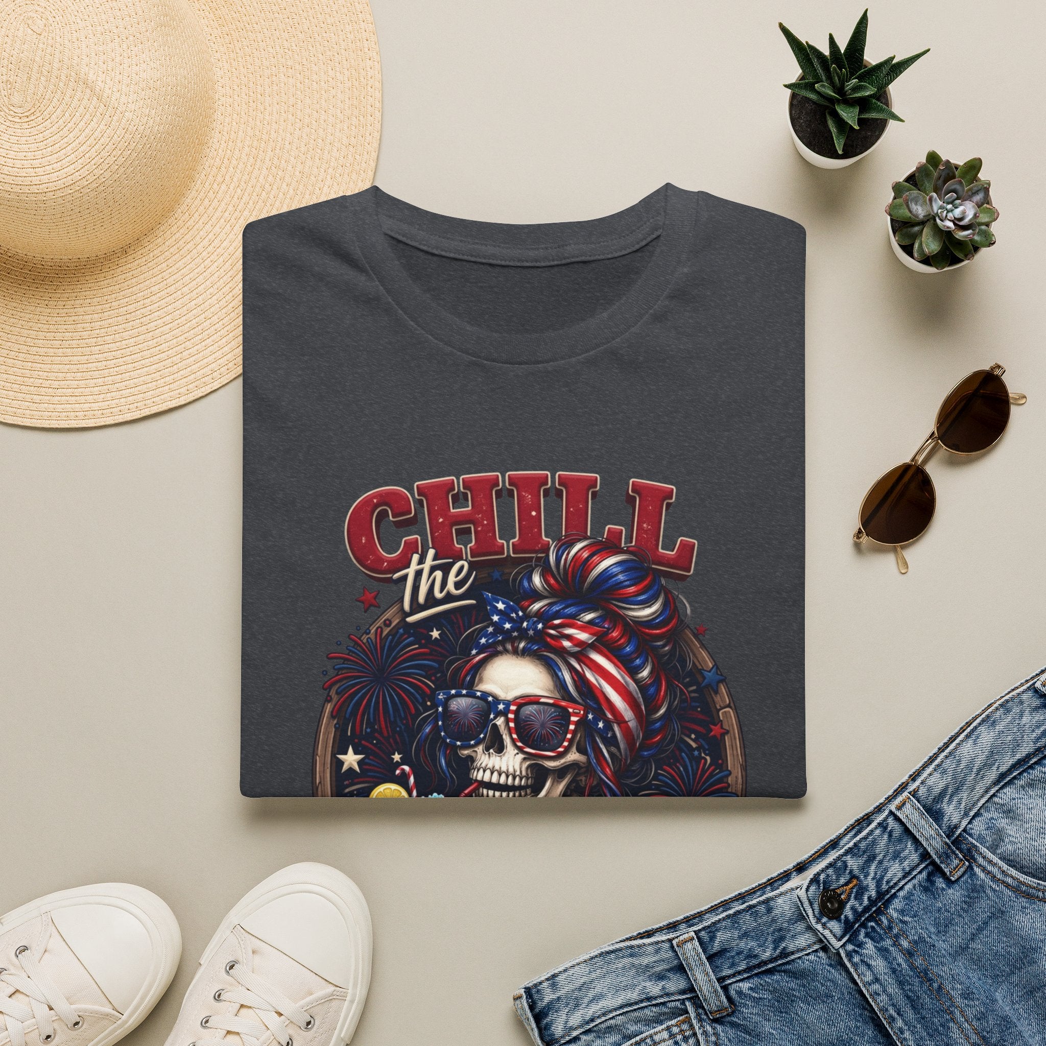Chill the Fourth Out Patriotic Skeleton 4th of July print on a Dark Heather Grey t-shirt, folded beside a straw hat and jeans