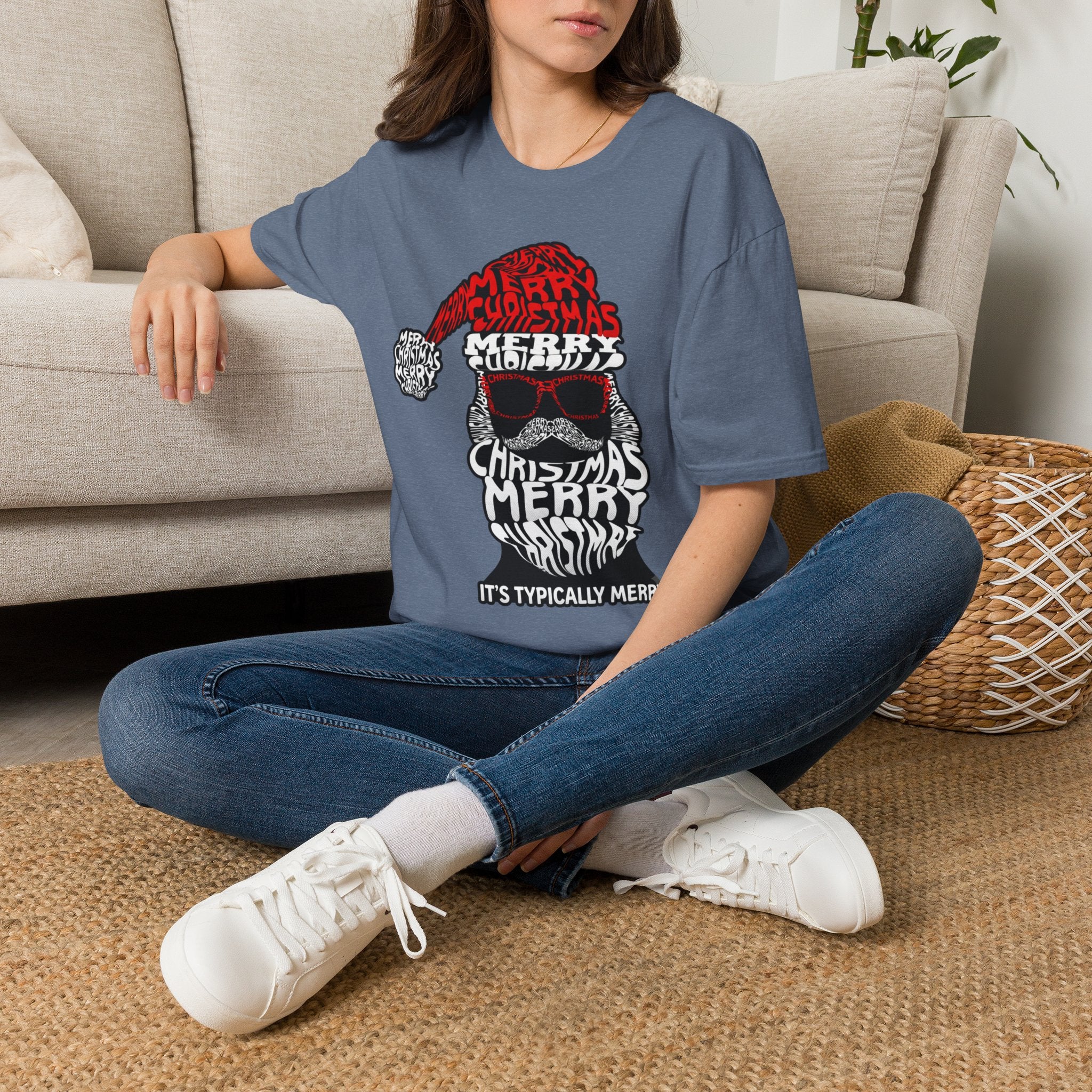 Cool Santa Sunglasses Typography Merry t-shirt in Heather Indigo, worn by a woman seated on a rug