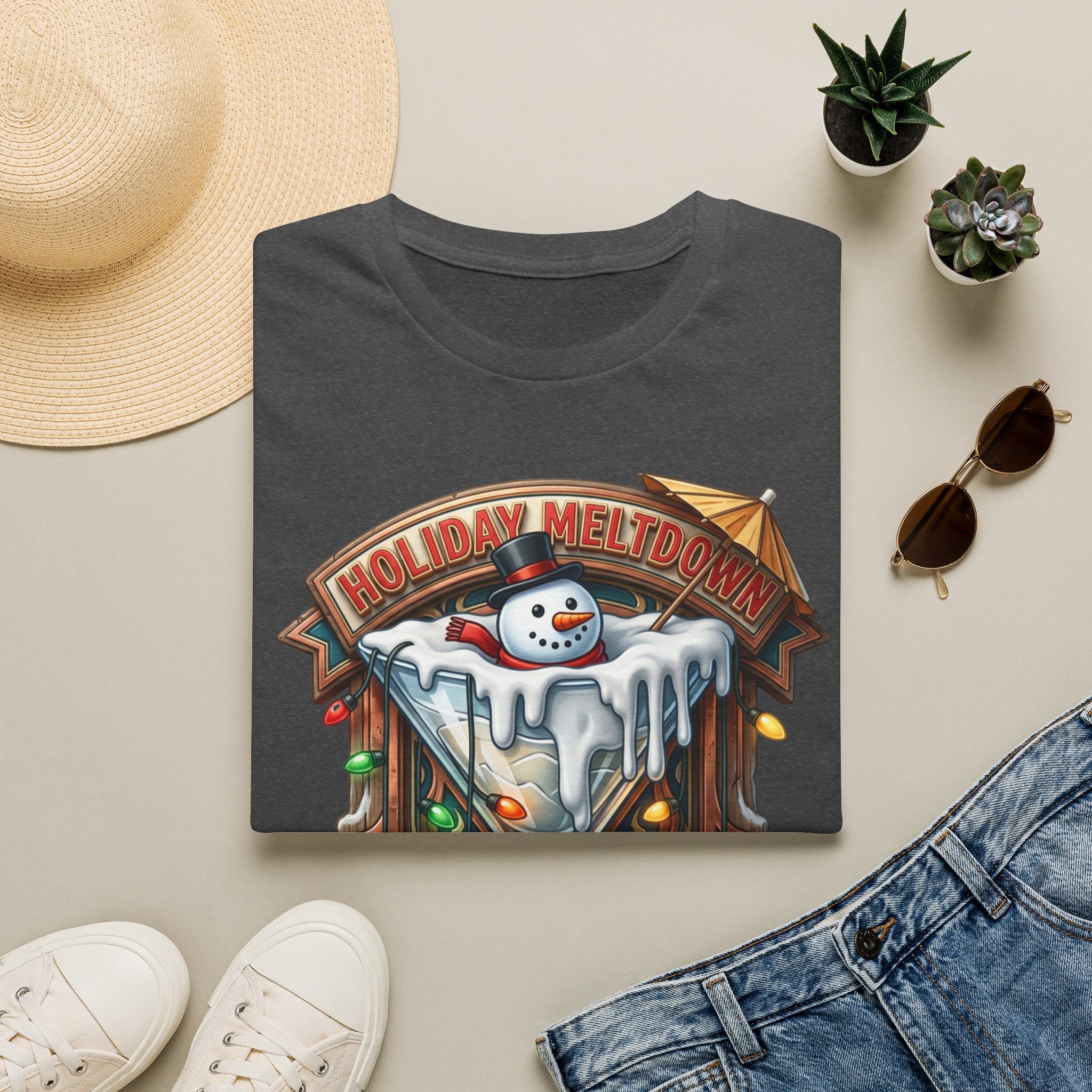 Holiday Meltdown Snowman Martini print on a Dark Heather t-shirt, folded beside a straw hat and jeans