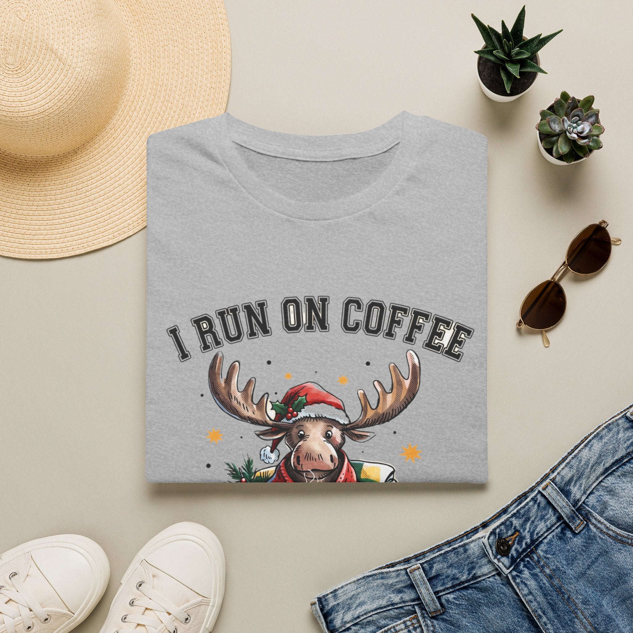Moose I Run On Coffee and Sleighin' It print on a Sport Grey t-shirt, folded beside a straw hat and jeans