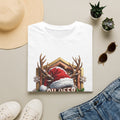 Oh Deer It's Christmas Looks a Lot Like Cocktails print on a White t-shirt, folded beside a straw hat and jeans