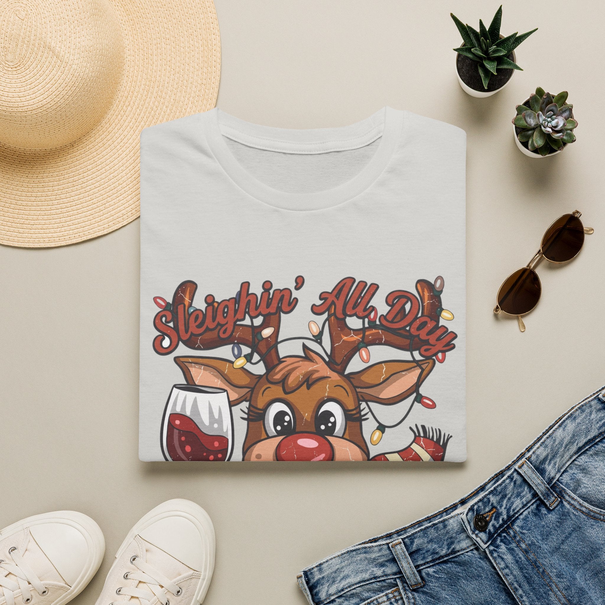 Reindeer Sleighin' All Day Tipsy All Night print on an Ice Grey t-shirt, folded beside a straw hat and jeans