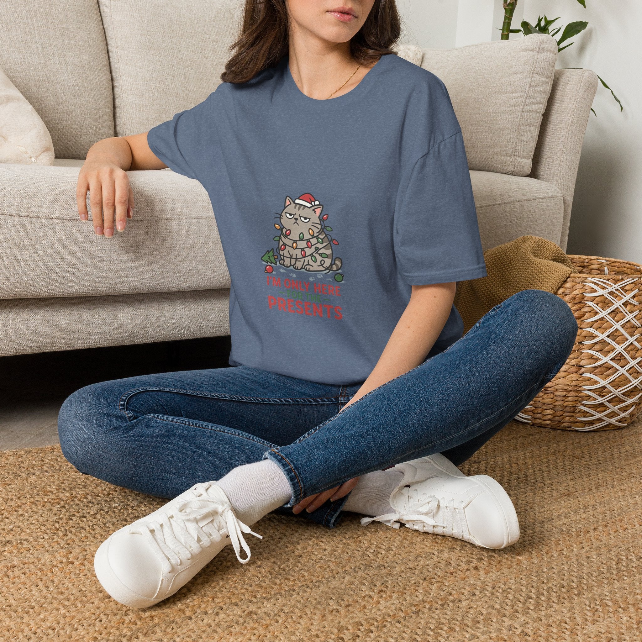 Funny Cat I'm Only Here for the Presents t-shirt in Heather Indigo, worn by a woman seated on a rug