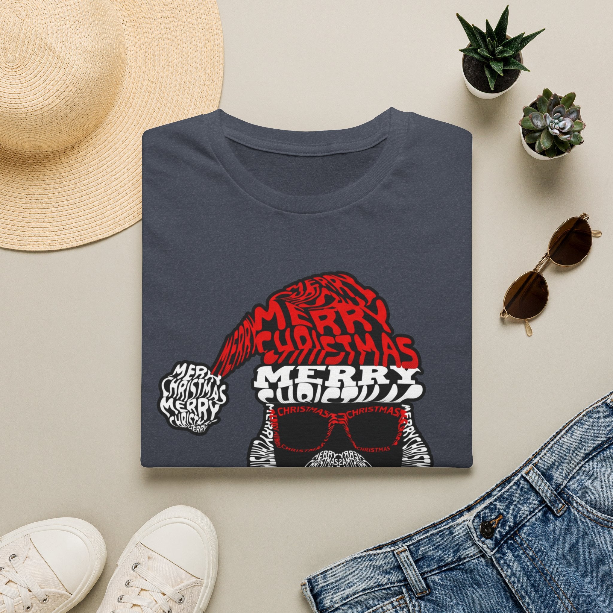Cool Santa Sunglasses Typography Merry print on a Heather Navy t-shirt, folded beside a straw hat and jeans