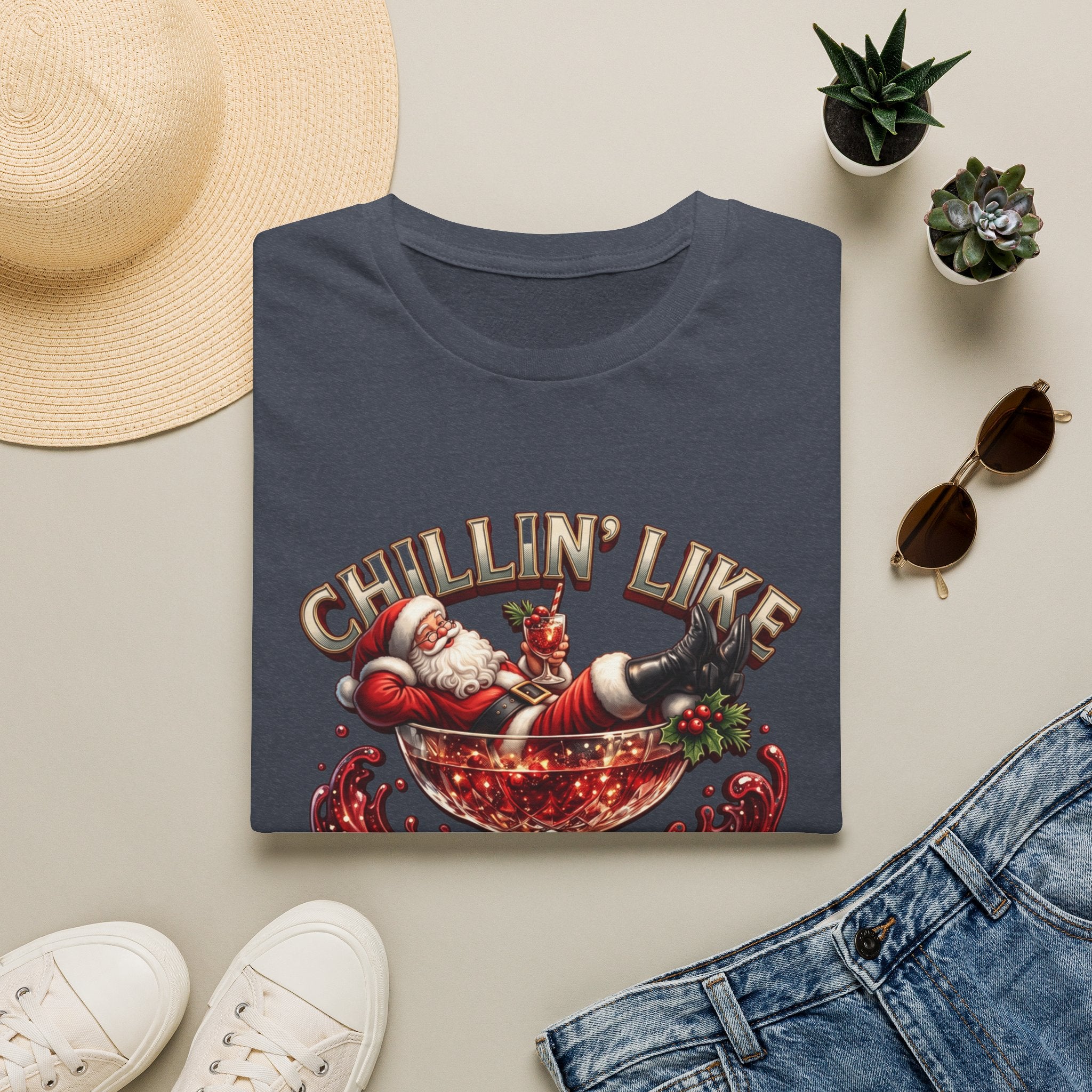 Chillin' Like a Kringle Santa print on a Heather Navy t-shirt, folded beside a straw hat and jeans