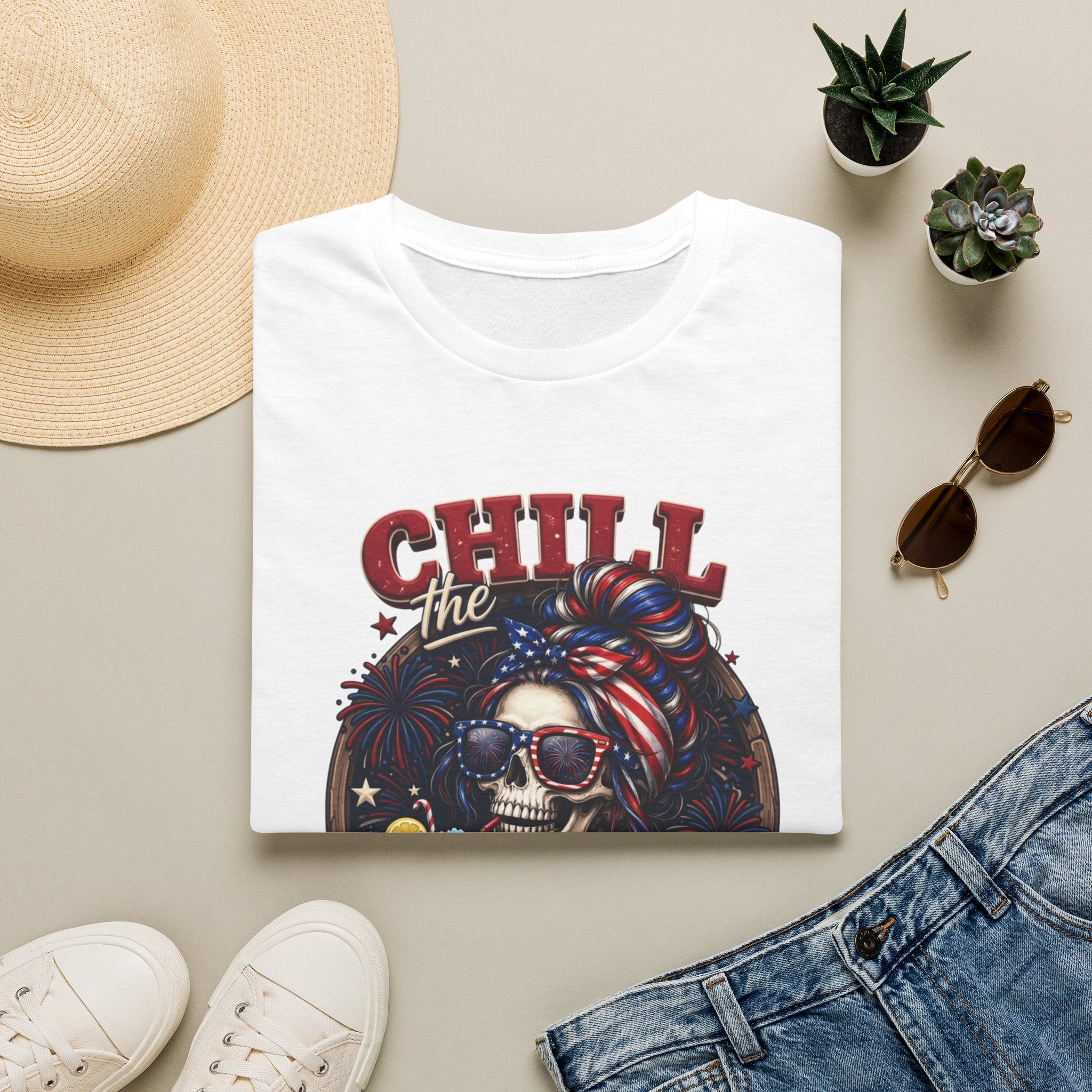 Chill the Fourth Out Patriotic Skeleton 4th of July print on a White t-shirt, folded beside a straw hat and jeans