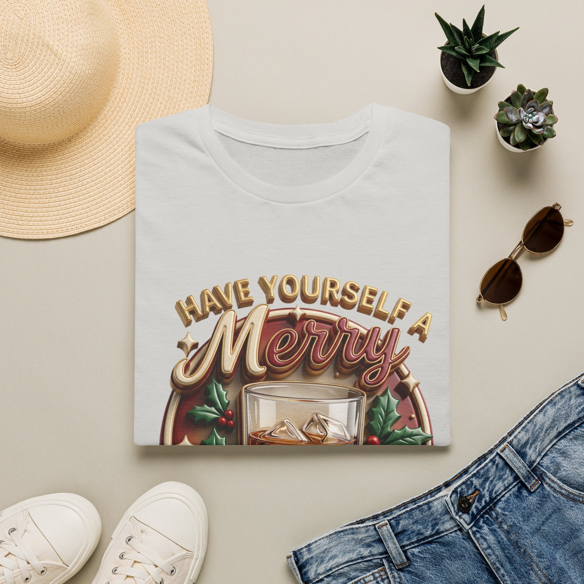 Have Yourself a Merry Little Cocktail print on an Ice Grey t-shirt, folded beside a straw hat and jeans