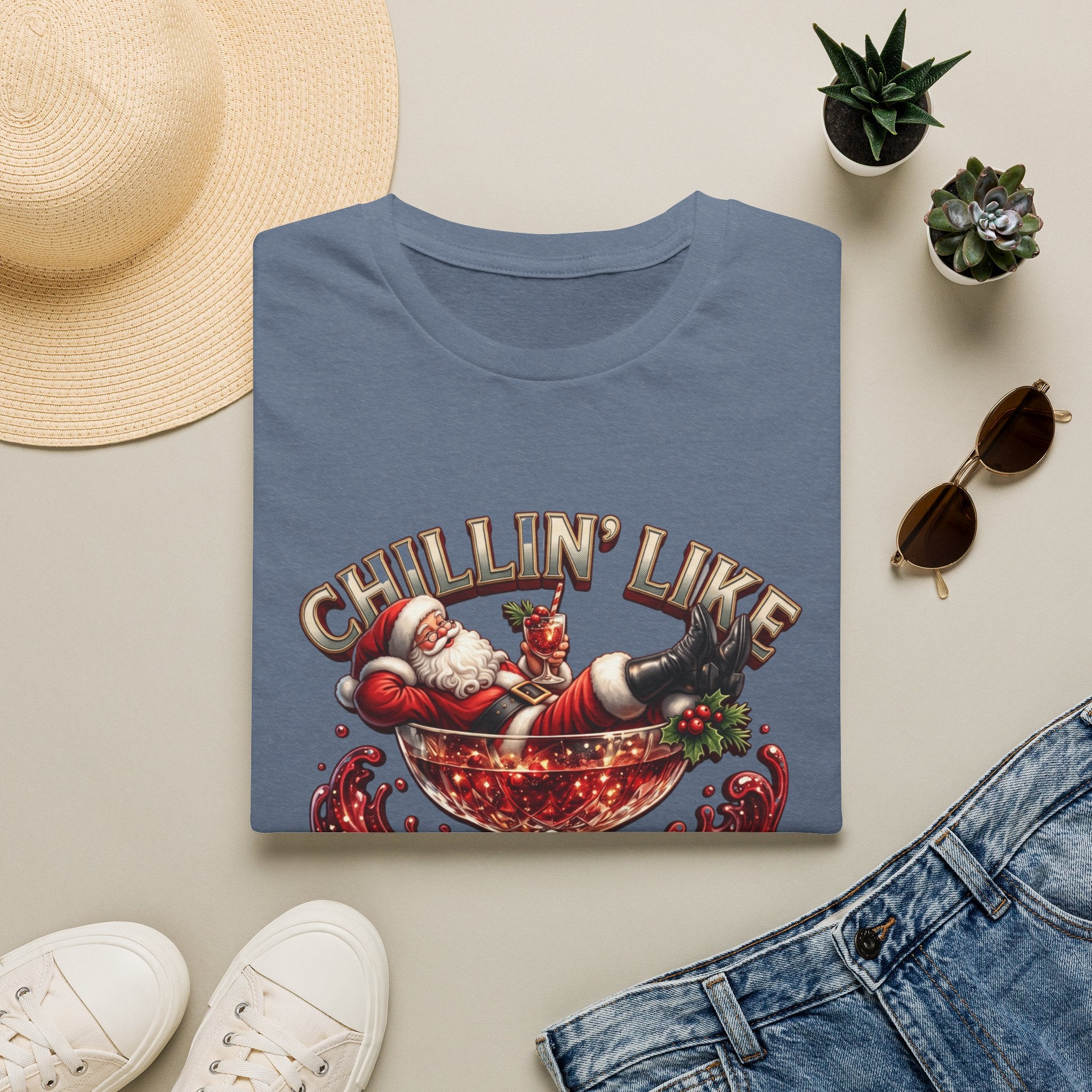 Chillin' Like a Kringle Santa print on a Heather Indigo t-shirt, folded beside a straw hat and jeans
