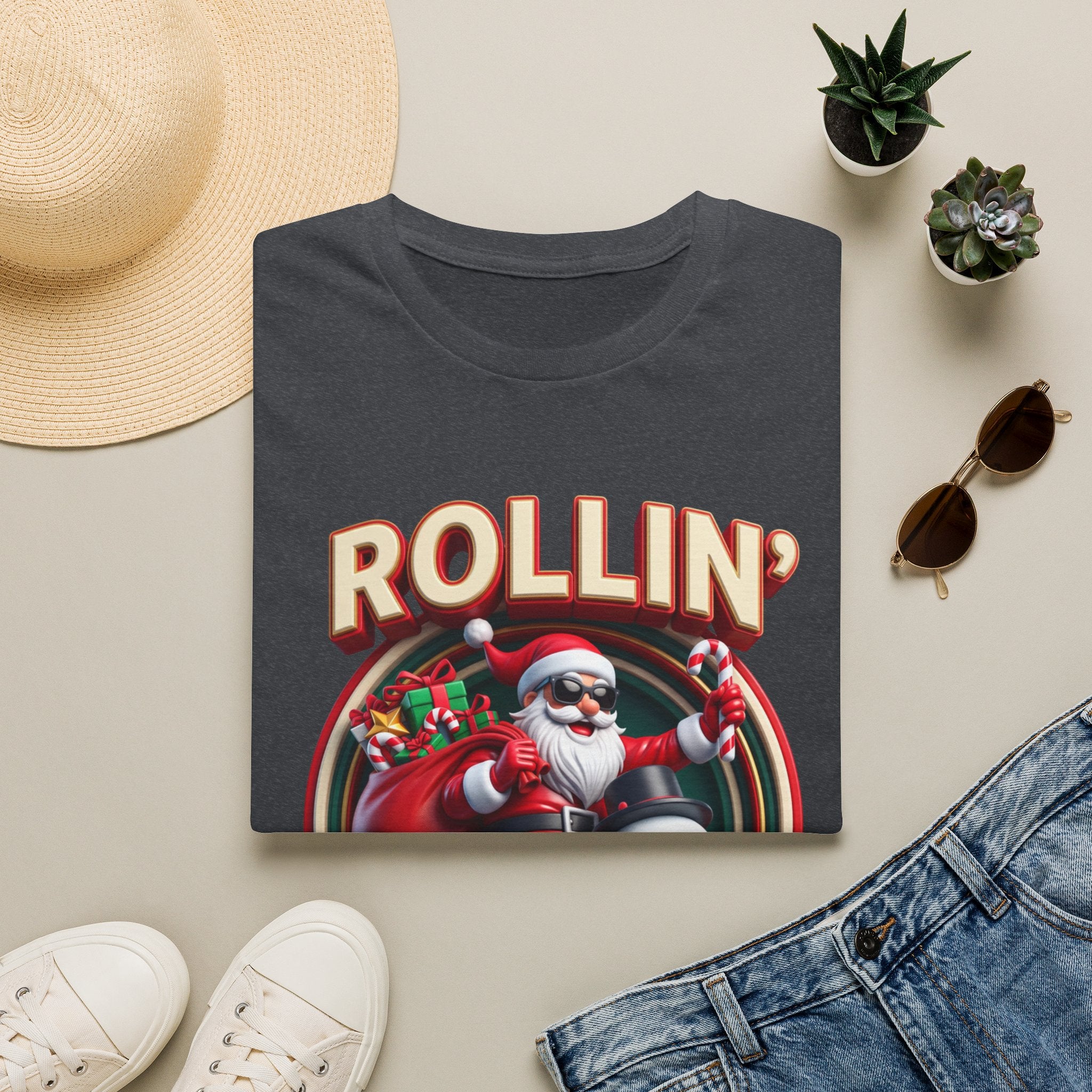 Rollin' with My Snowmies Santa & Snowman print on a Dark Heather Grey t-shirt, folded beside a straw hat and jeans