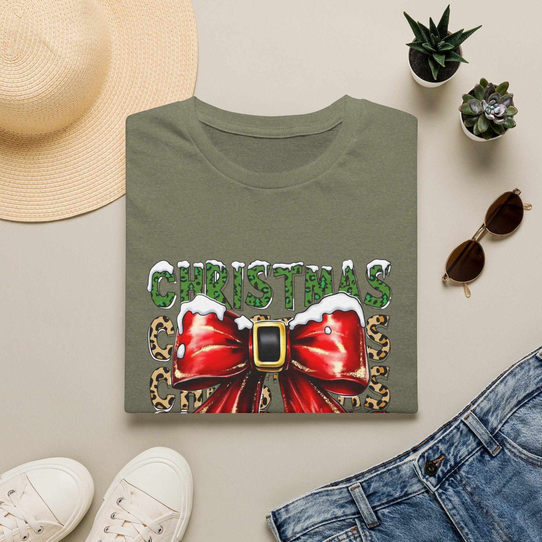 Stacked Christmas Leopard Print Santa Belt Bow print on a Heather Military Green t-shirt, folded beside a straw hat and jeans