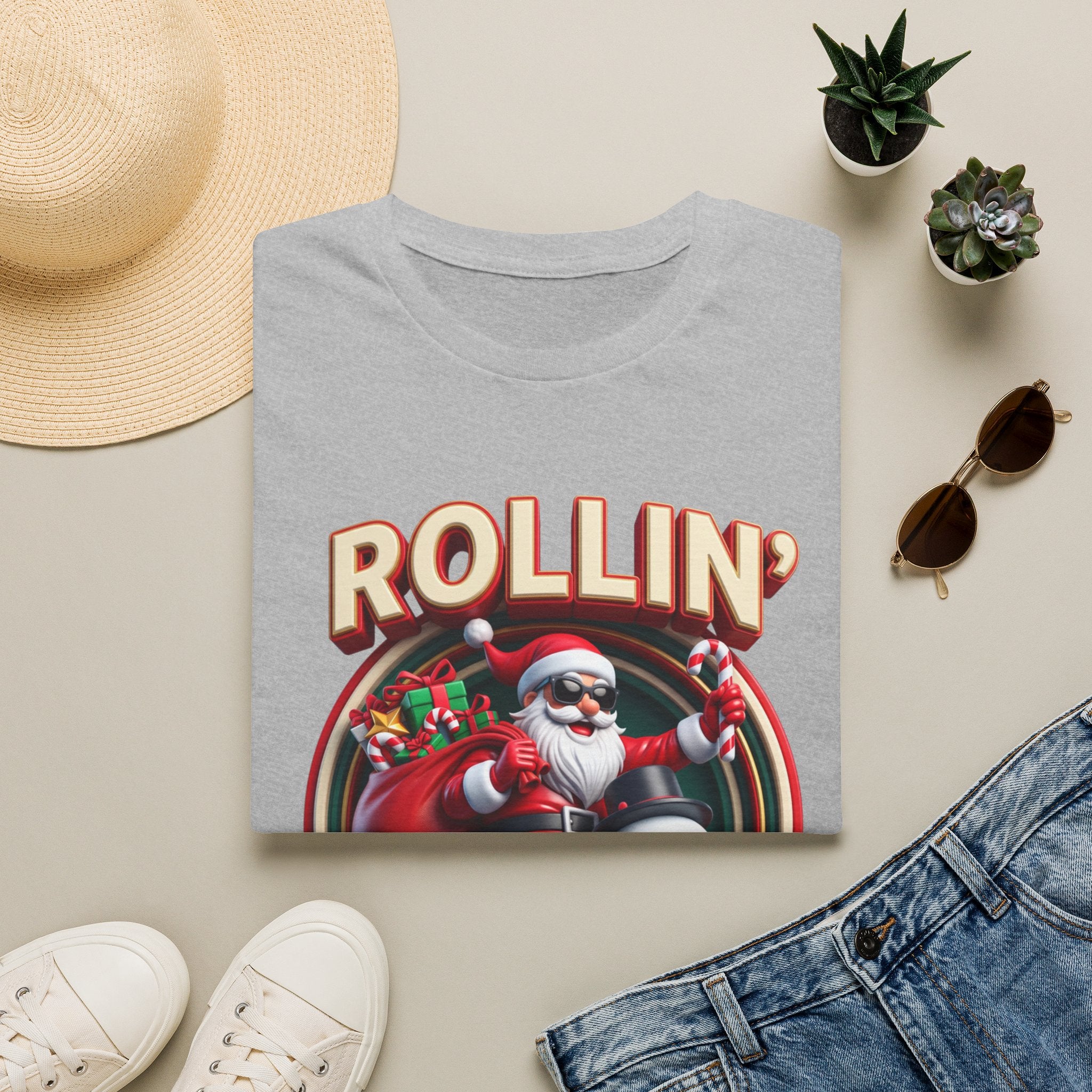 Rollin' with My Snowmies Santa & Snowman print on a Sport Grey t-shirt, folded beside a straw hat and jeans