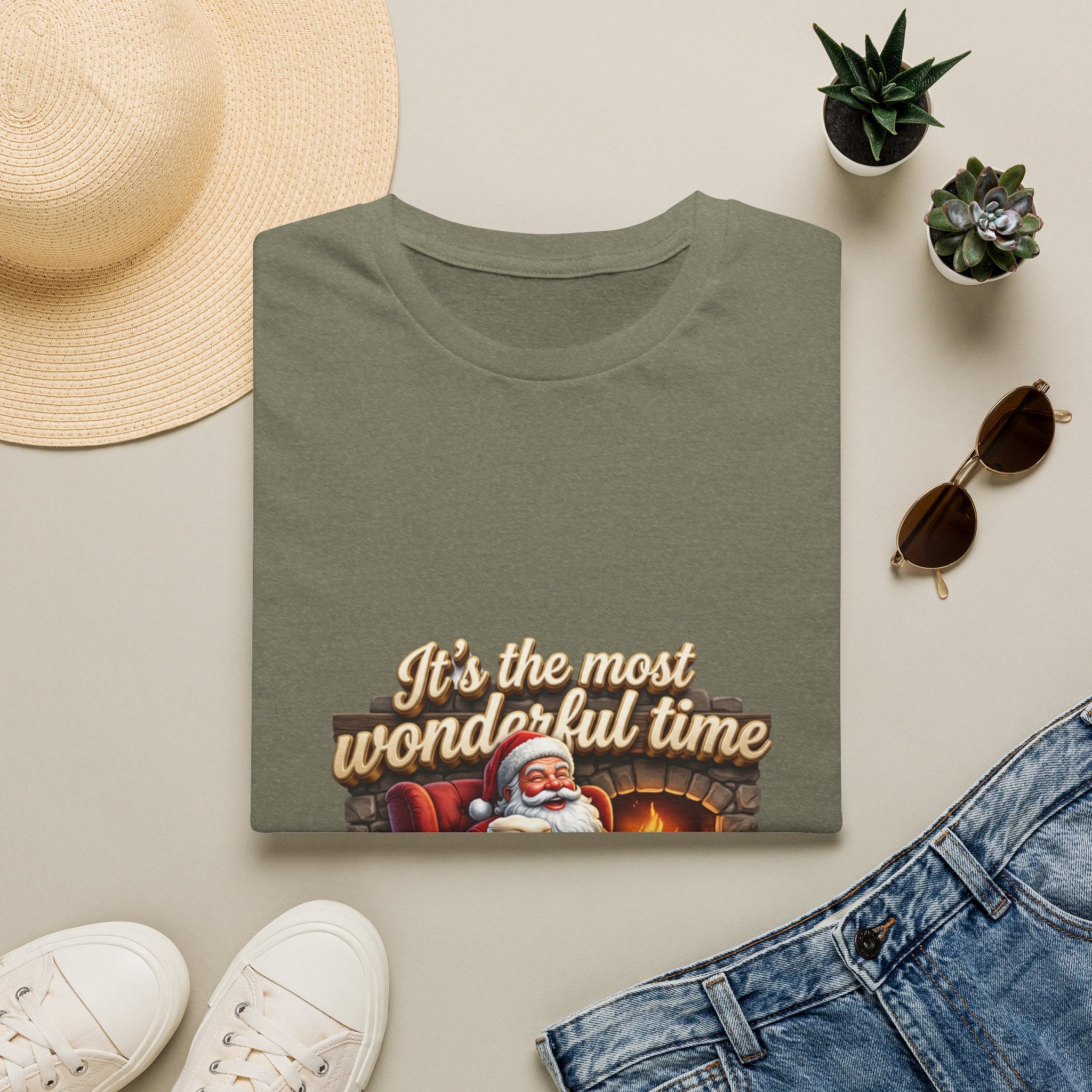 Most Wonderful Time for a Beer Santa print on a Heather Military Green t-shirt, folded beside a straw hat and jeans