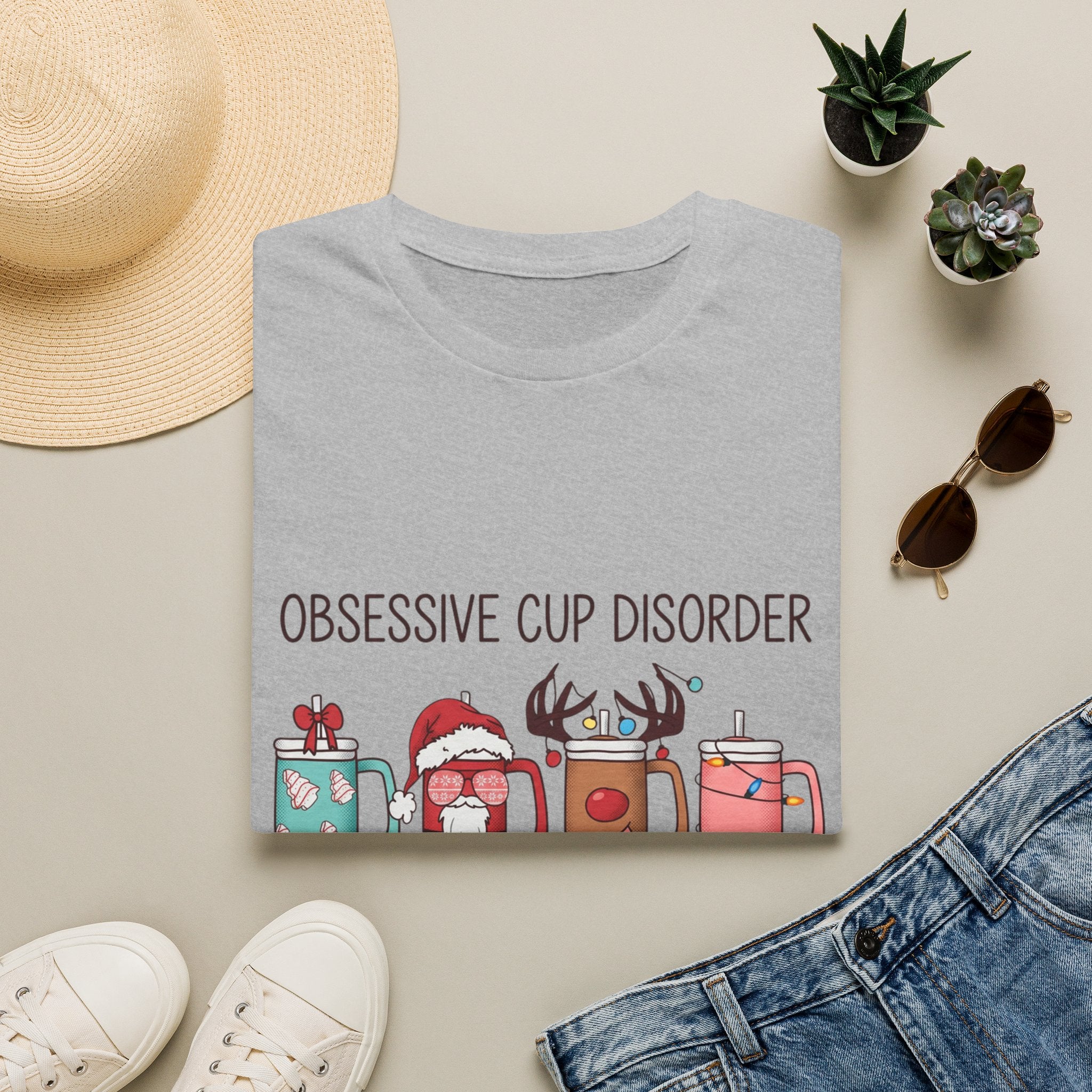 Obsessive Cup Disorder Funny Christmas Tumbler print on a Sport Grey t-shirt, folded beside a straw hat and jeans