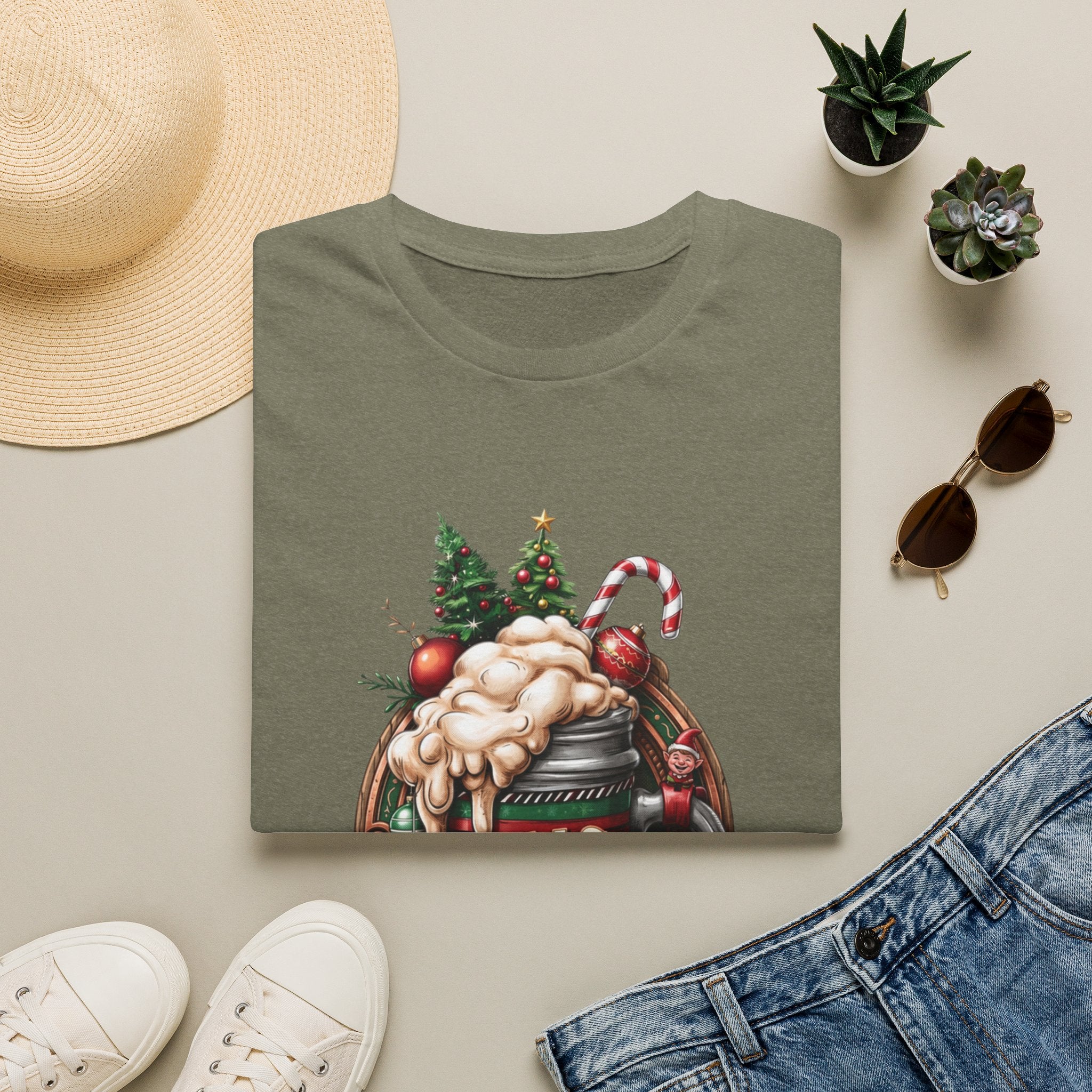 XMAS Beer Pour Me a Very Merry Christmas print on a Heather Military Green t-shirt, folded beside a straw hat and jeans