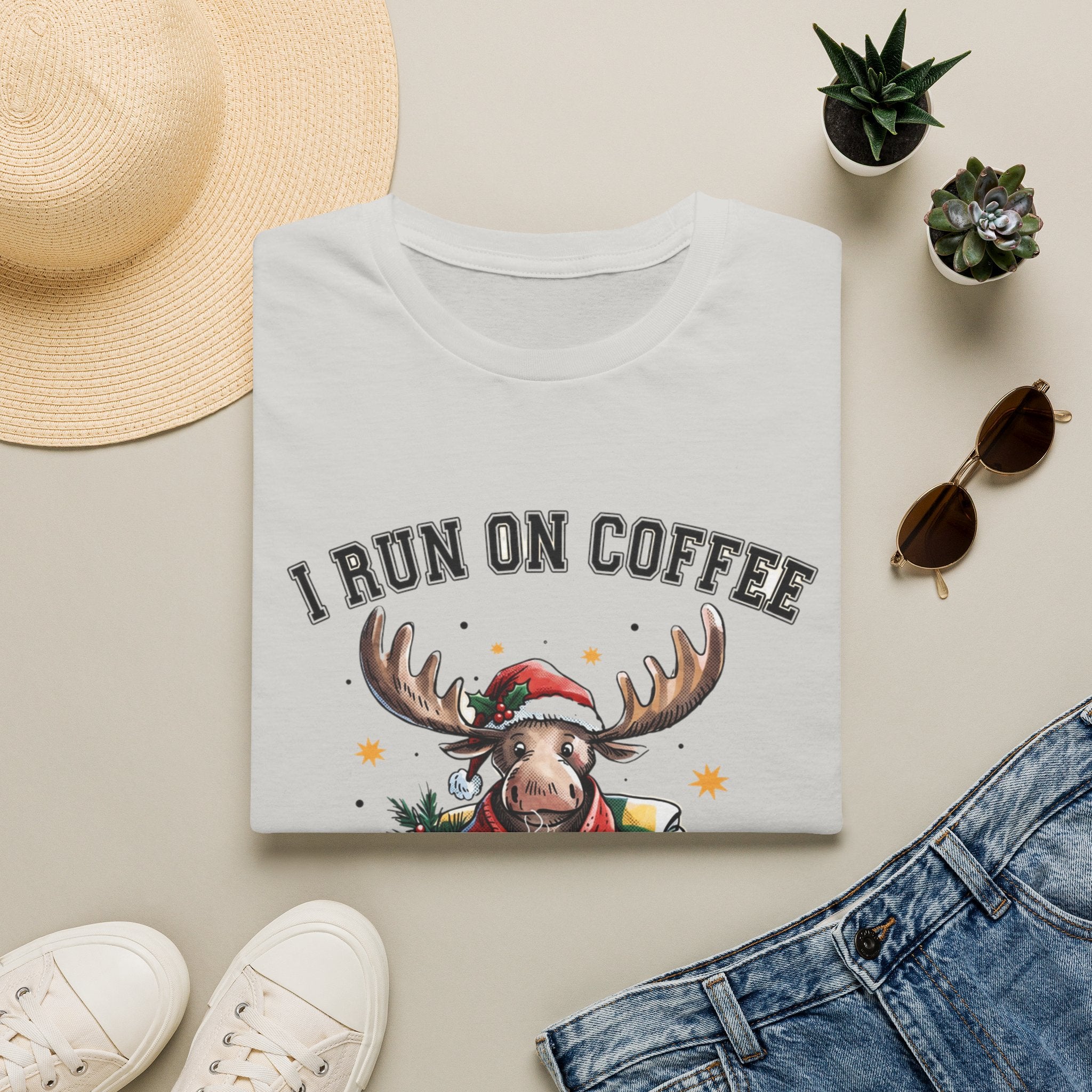Moose I Run On Coffee and Sleighin' It print on an Ice Grey t-shirt, folded beside a straw hat and jeans