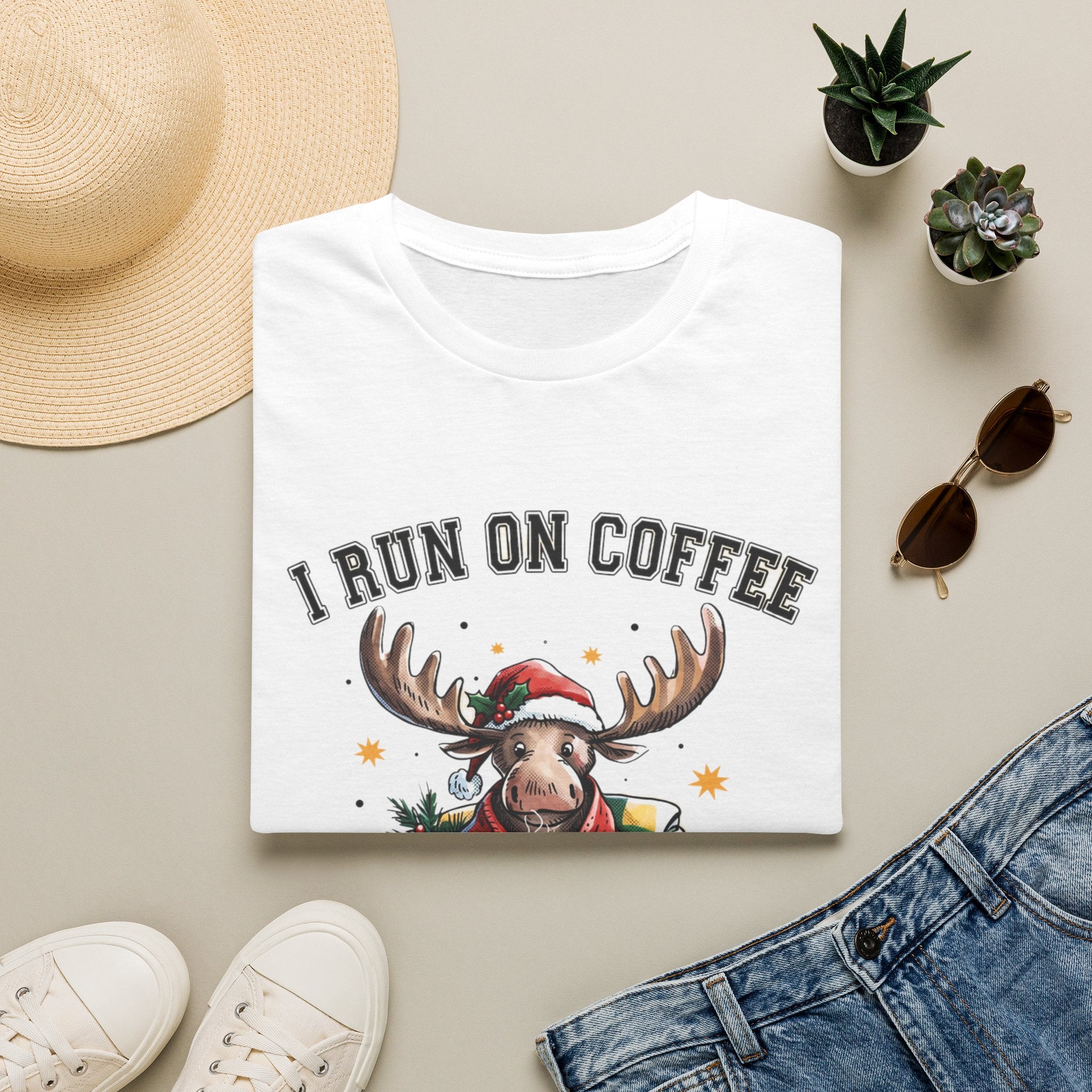 Moose I Run On Coffee and Sleighin' It print on a White t-shirt, folded beside a straw hat and jeans