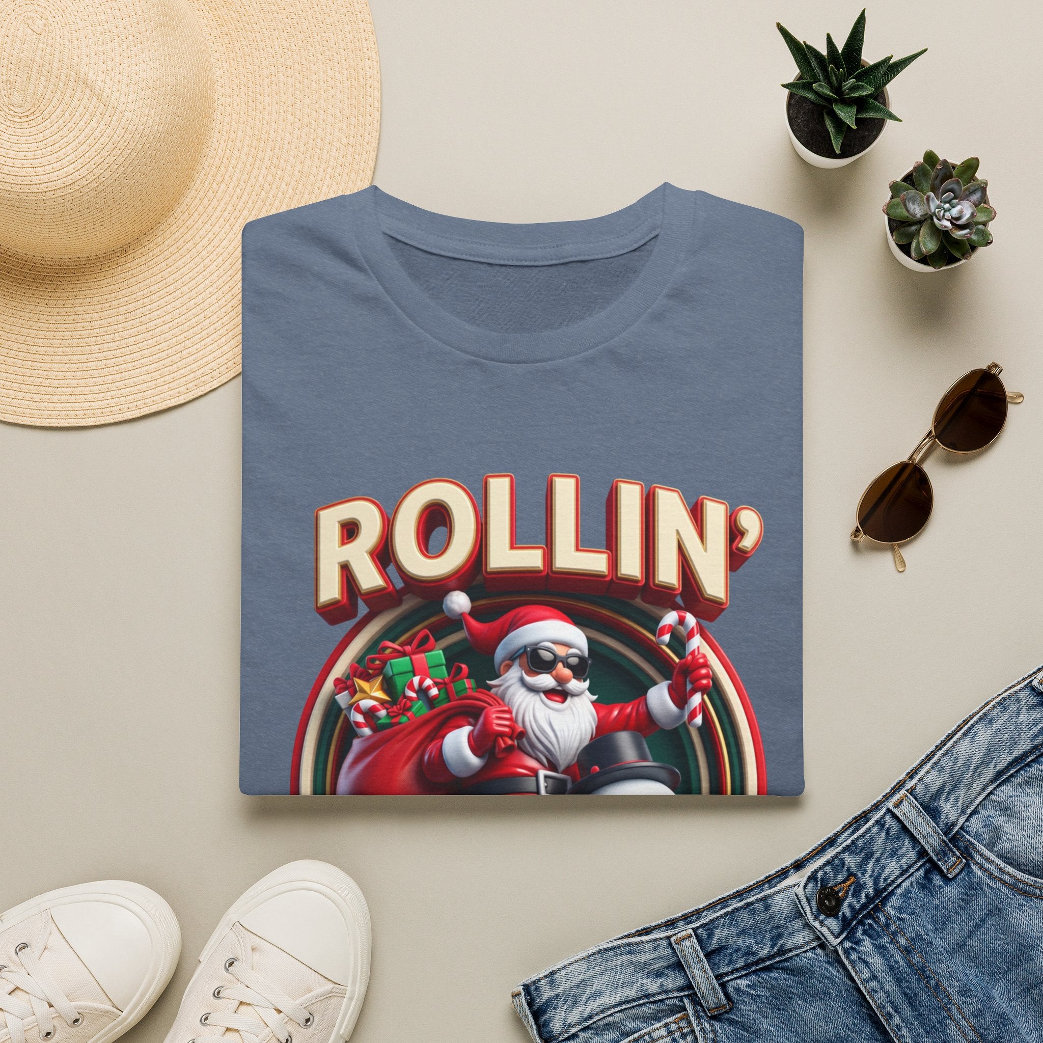 Rollin' with My Snowmies Santa & Snowman print on a Heather Indigo t-shirt, folded beside a straw hat and jeans