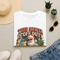 This Santa Is Off Duty Cocktail Club print on a White t-shirt, folded beside a straw hat and jeans