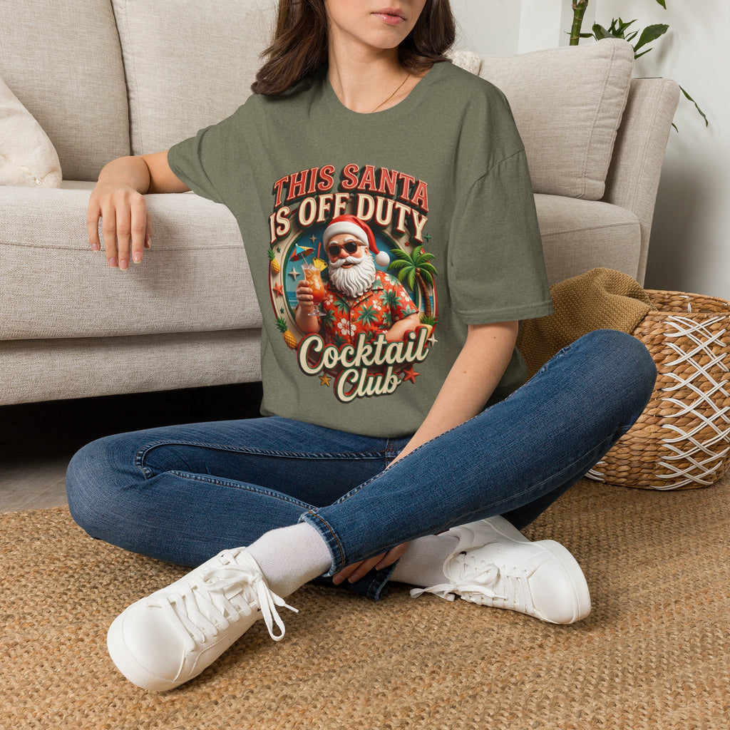 This Santa Is Off Duty Cocktail Club t-shirt in Heather Military Green, worn by a woman seated on a rug