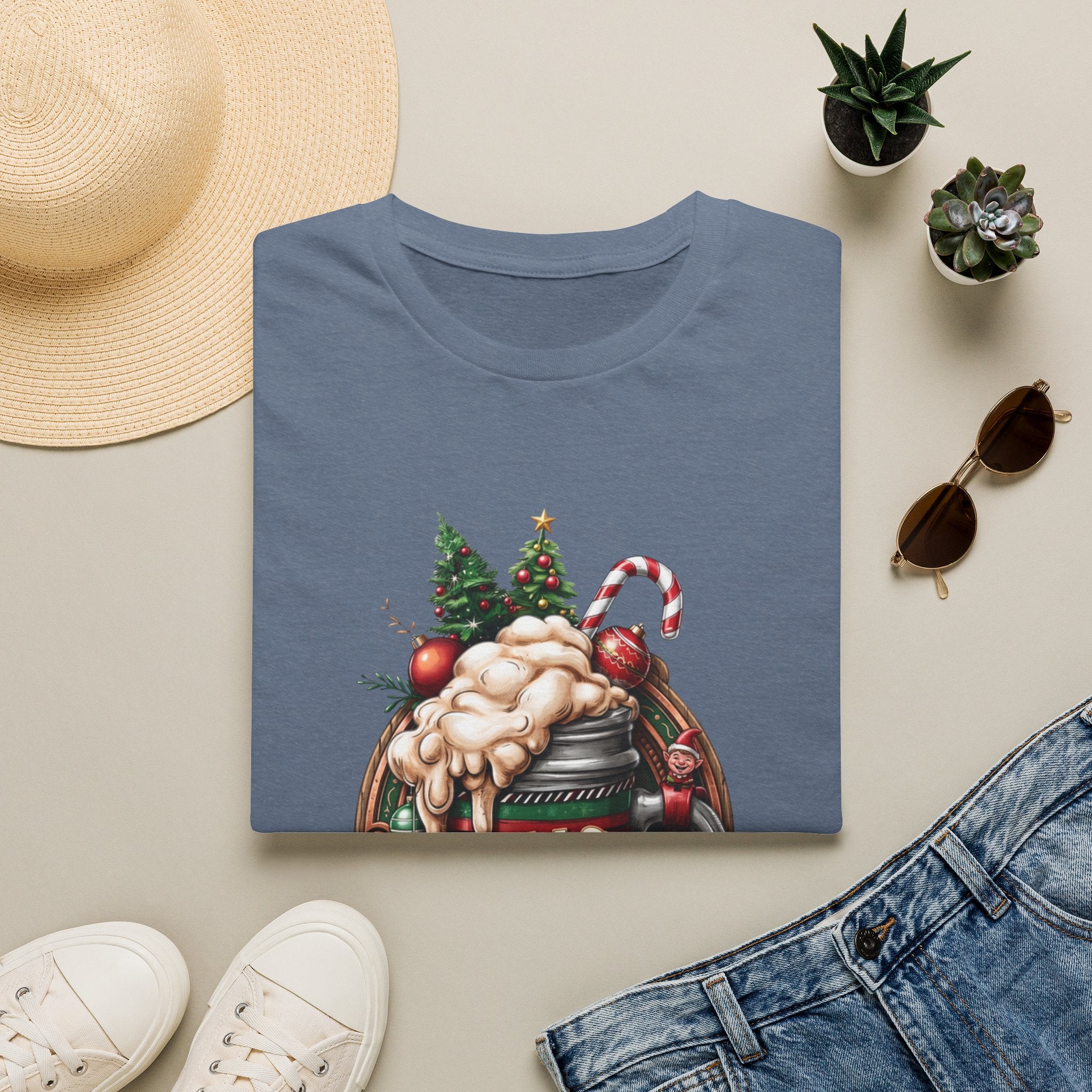 XMAS Beer Pour Me a Very Merry Christmas print on a Heather Indigo t-shirt, folded beside a straw hat and jeans