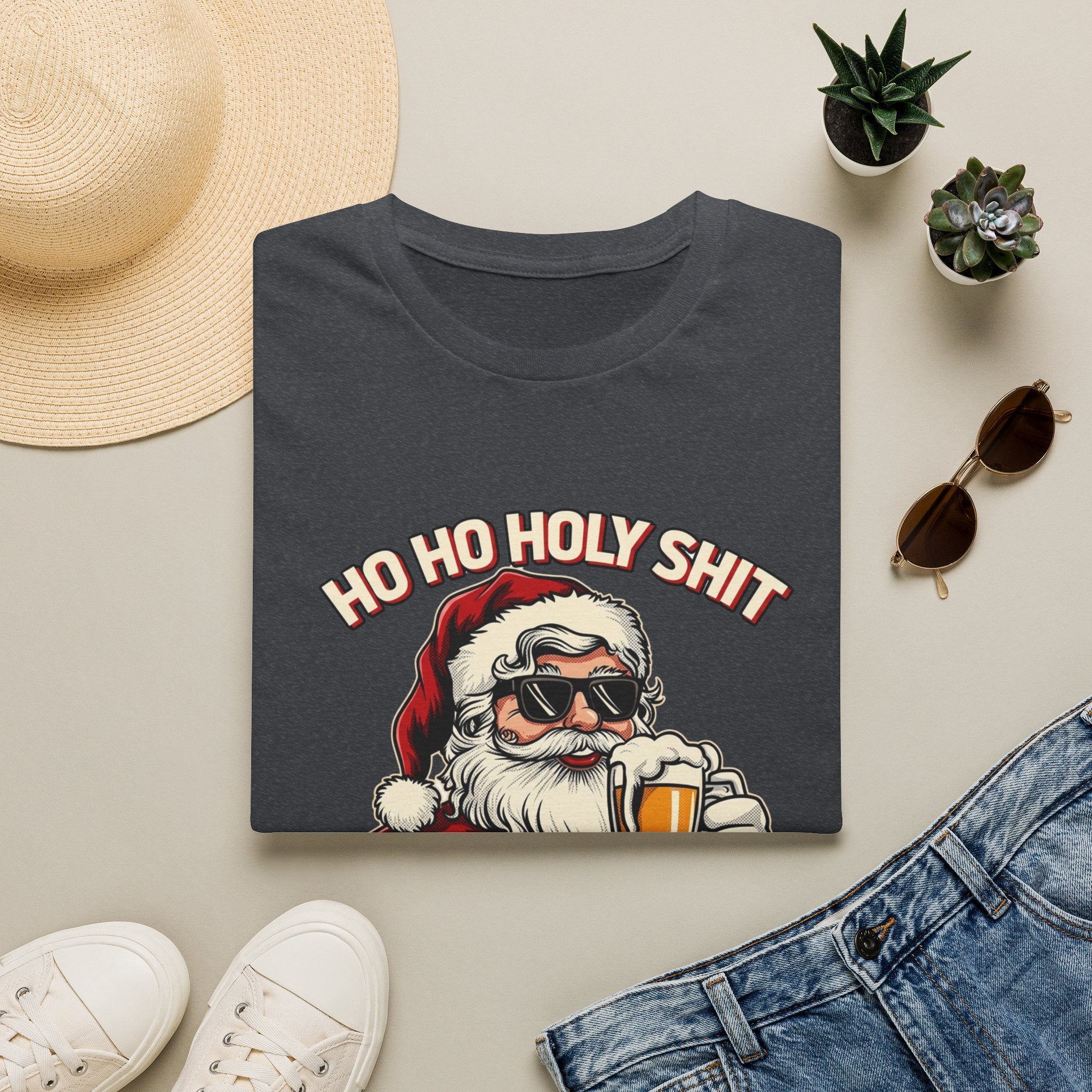 Ho Ho Holy Sh*t I Need a Beer print on a Dark Heather Grey t-shirt, folded beside a straw hat and jeans