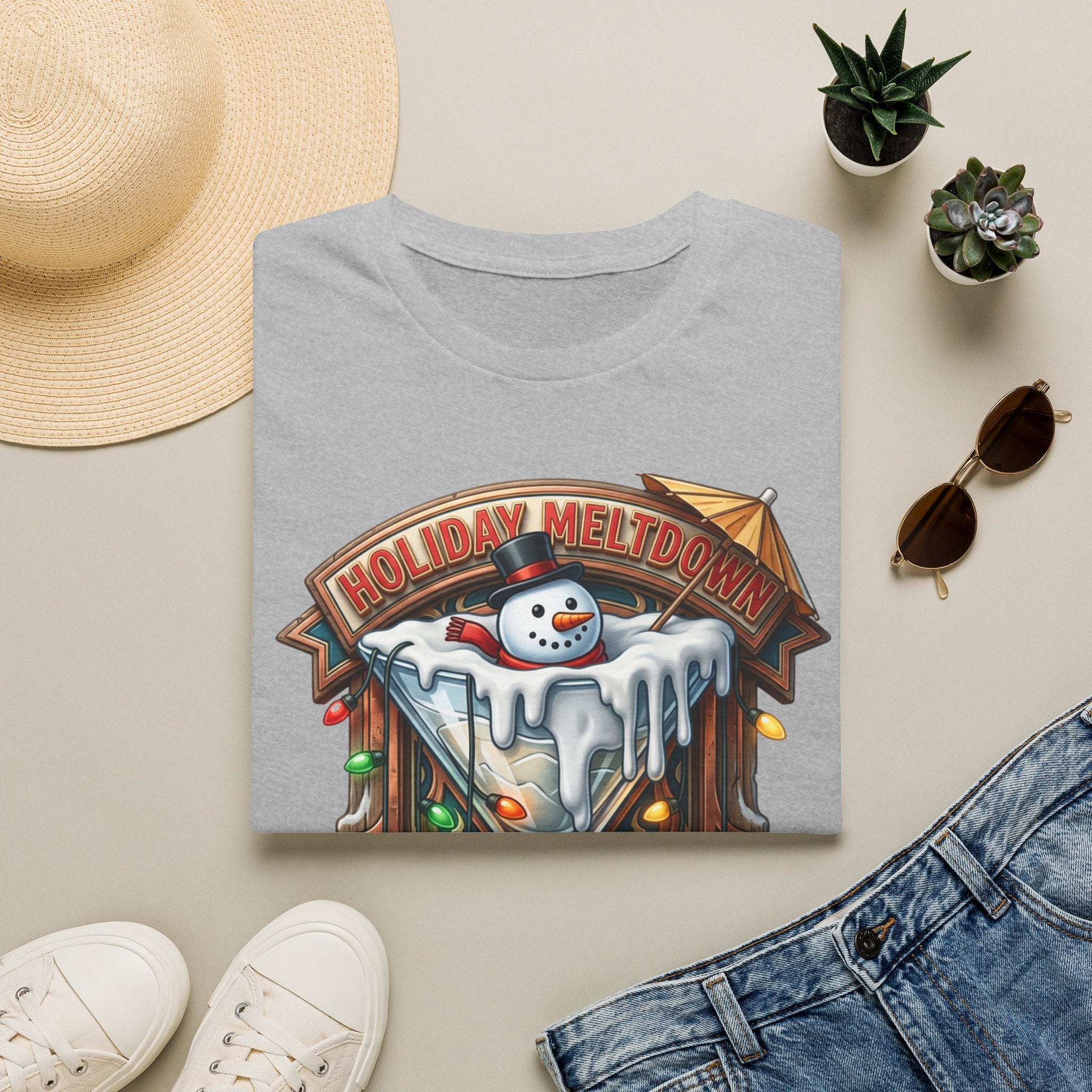 Holiday Meltdown Snowman Martini print on a Sport Grey t-shirt, folded beside a straw hat and jeans