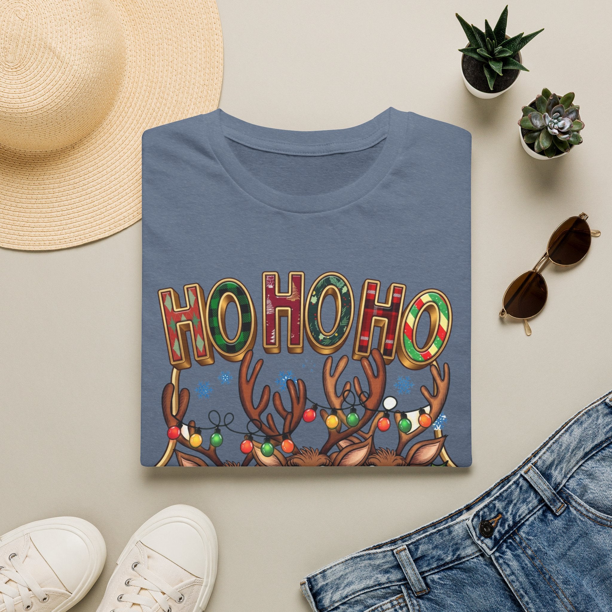 Reindeer Trio Ho Ho Ho Christmas Lights print on a Heather Indigo t-shirt, folded beside a straw hat and jeans