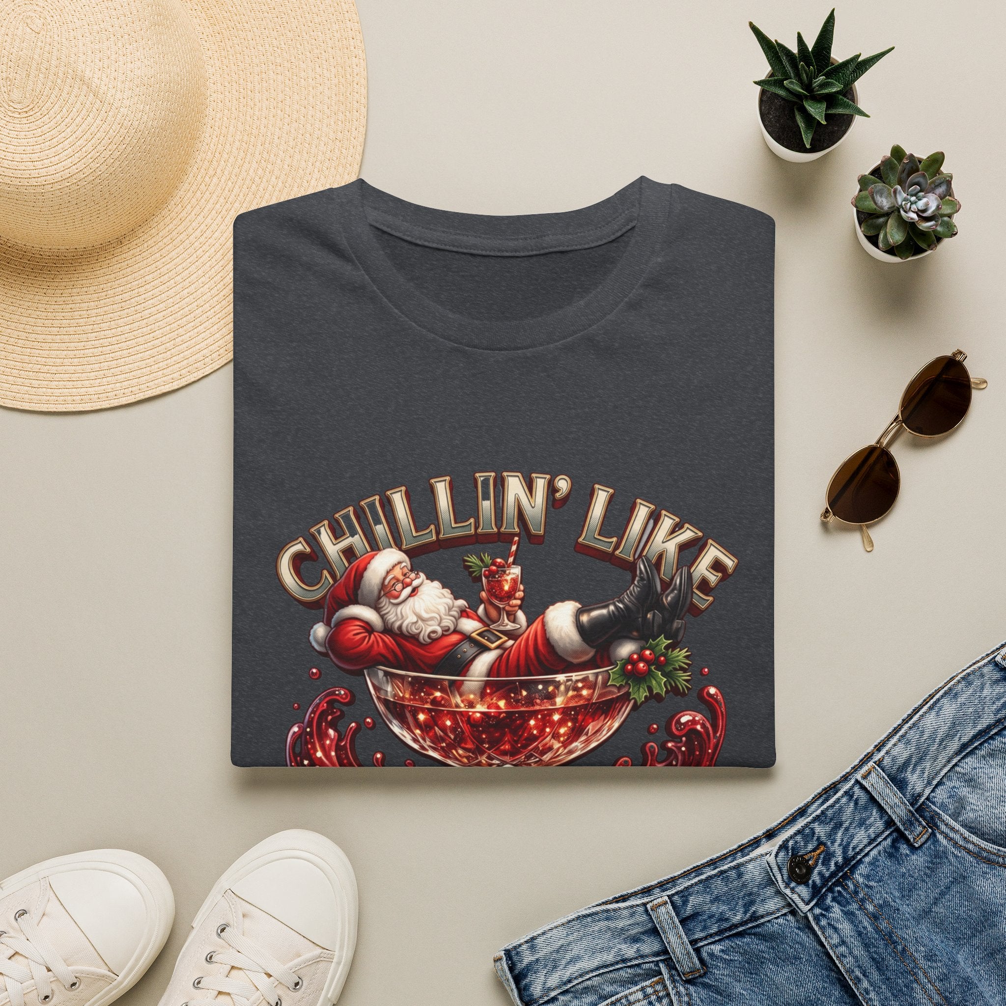 Chillin' Like a Kringle Santa print on a Dark Heather Grey t-shirt, folded beside a straw hat and jeans