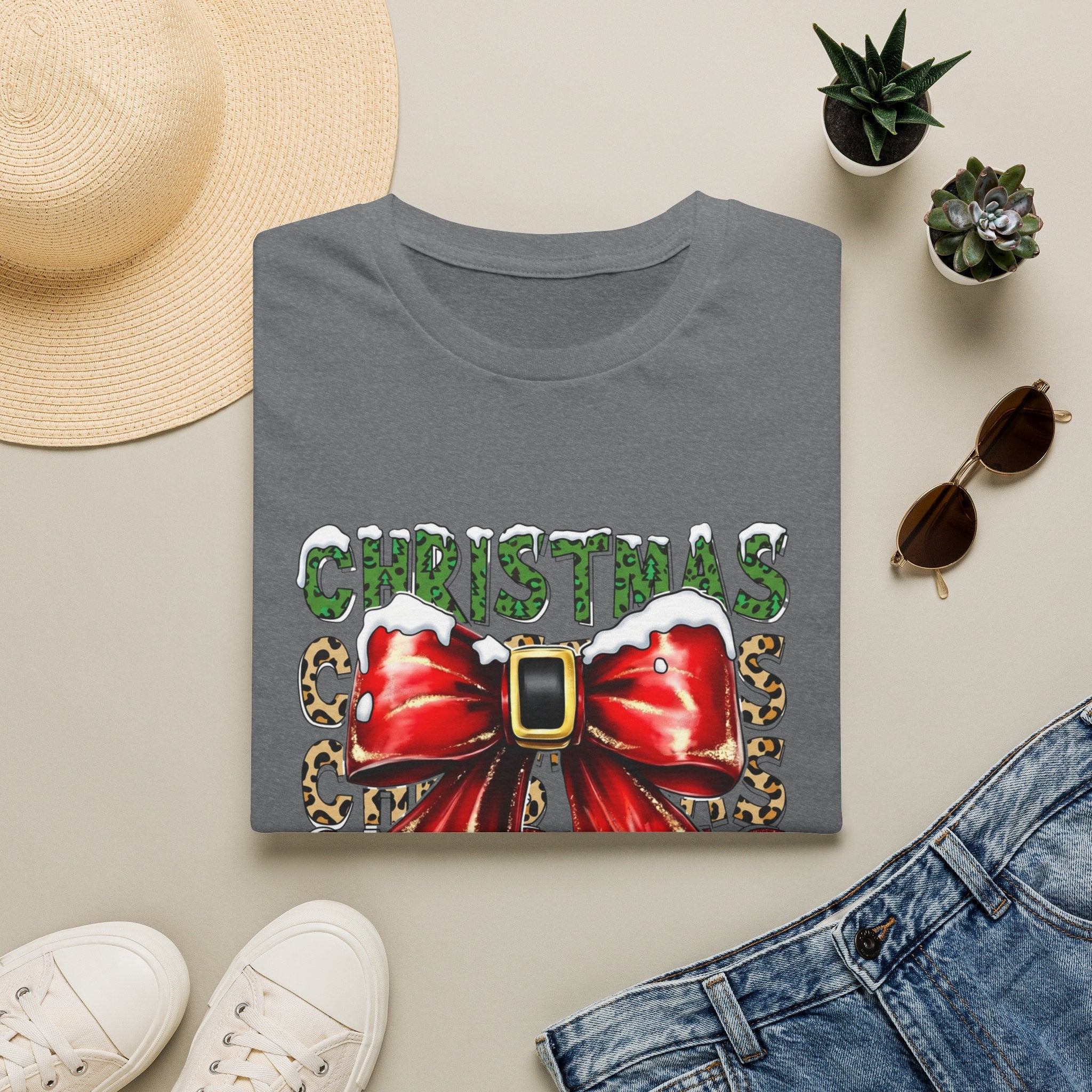 Stacked Christmas Leopard Print Santa Belt Bow print on a Graphite Heather t-shirt, folded beside a straw hat and jeans