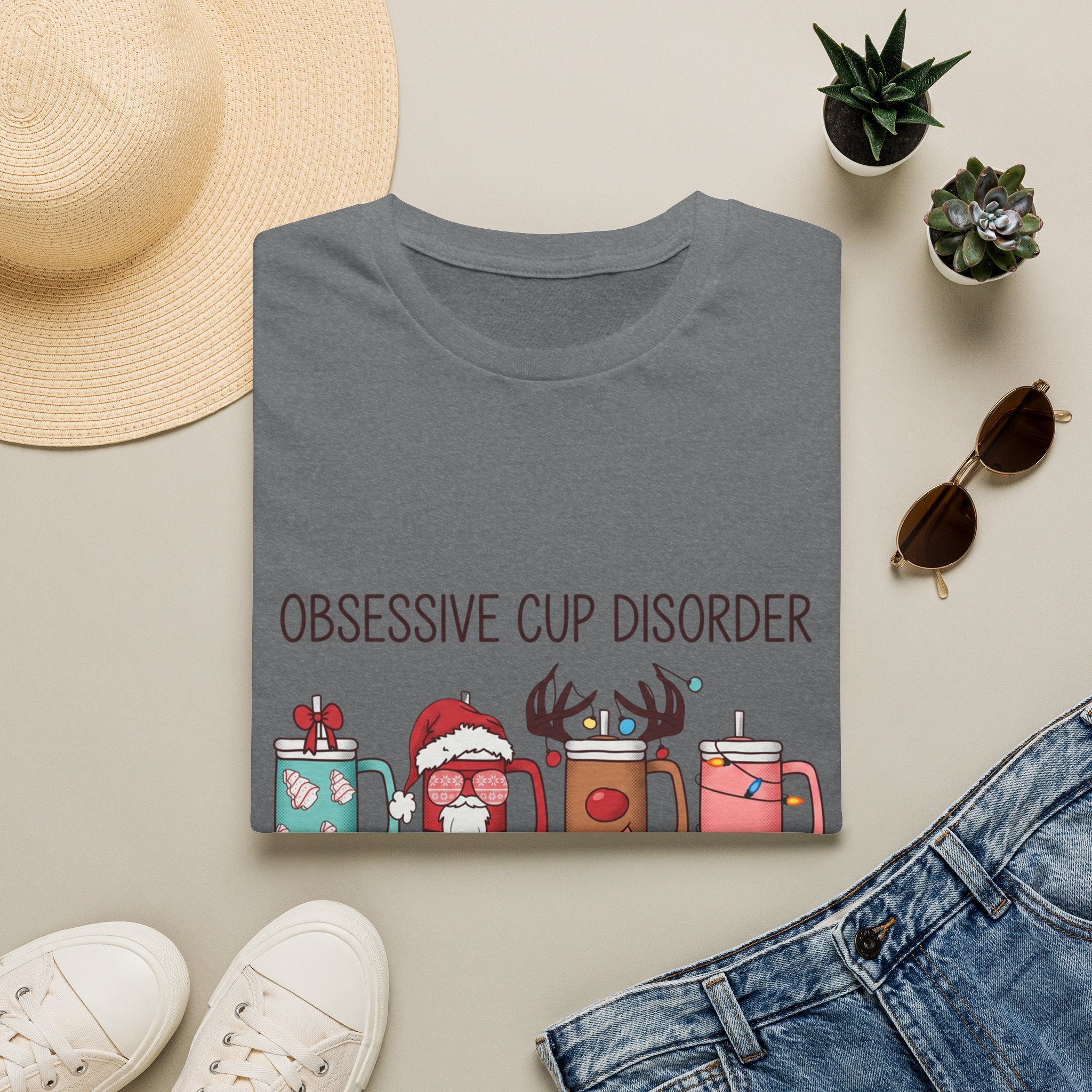 Obsessive Cup Disorder Funny Christmas Tumbler print on a Graphite Heather t-shirt, folded beside a straw hat and jeans