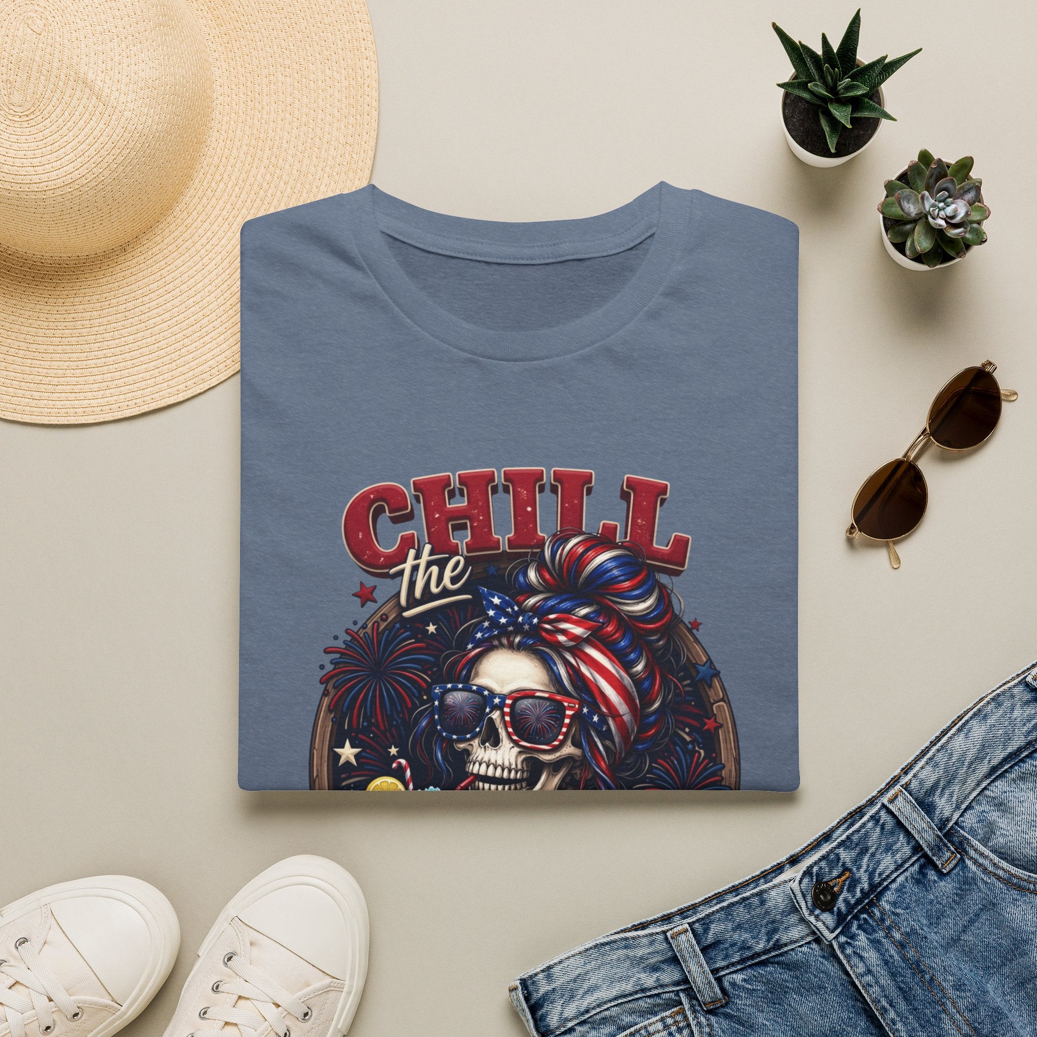 Chill the Fourth Out Patriotic Skeleton 4th of July print on a Heather Indigo t-shirt, folded beside a straw hat and jeans